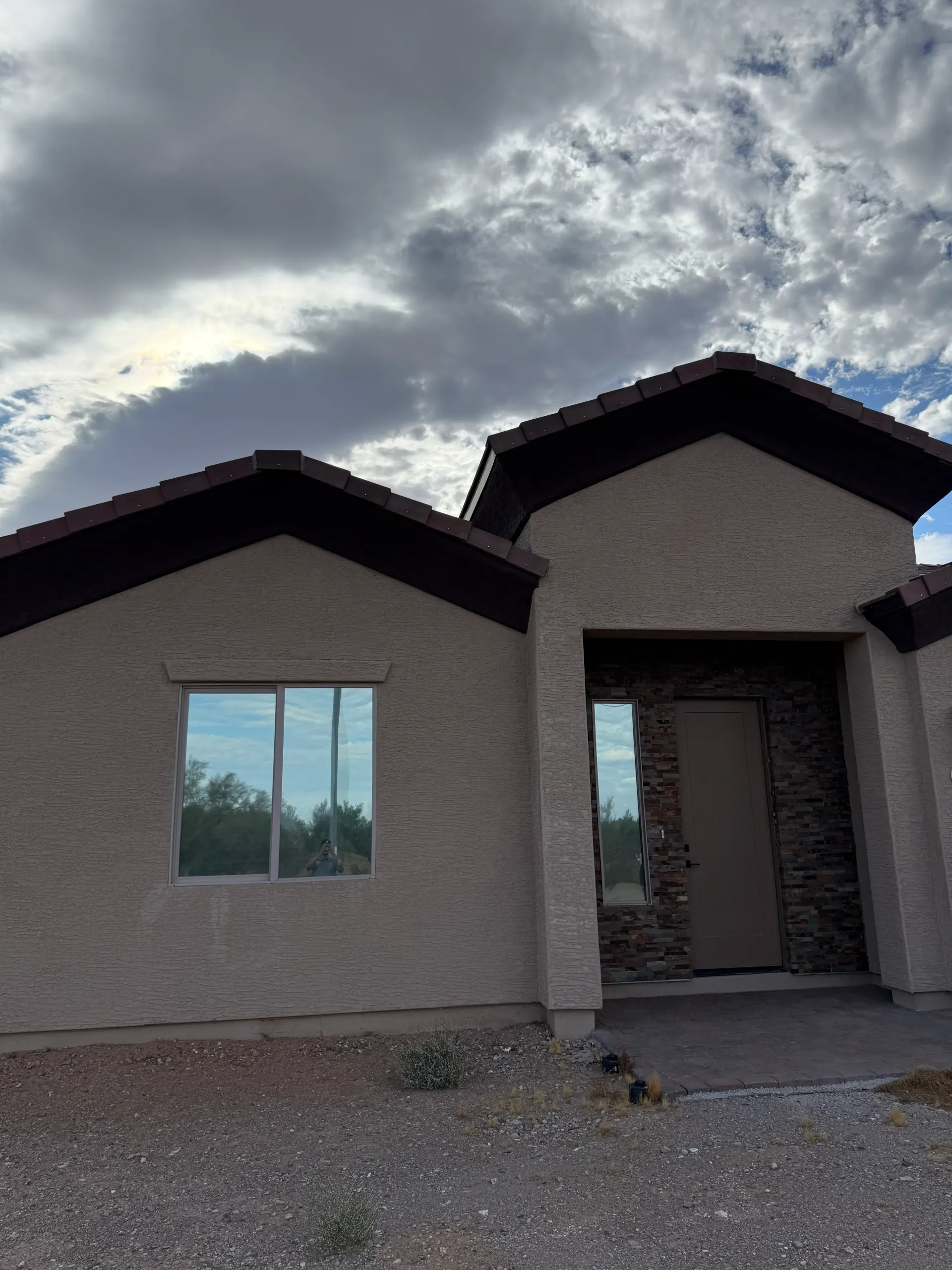 Tan stucco house with dark roof and trim, under cloudy sky.