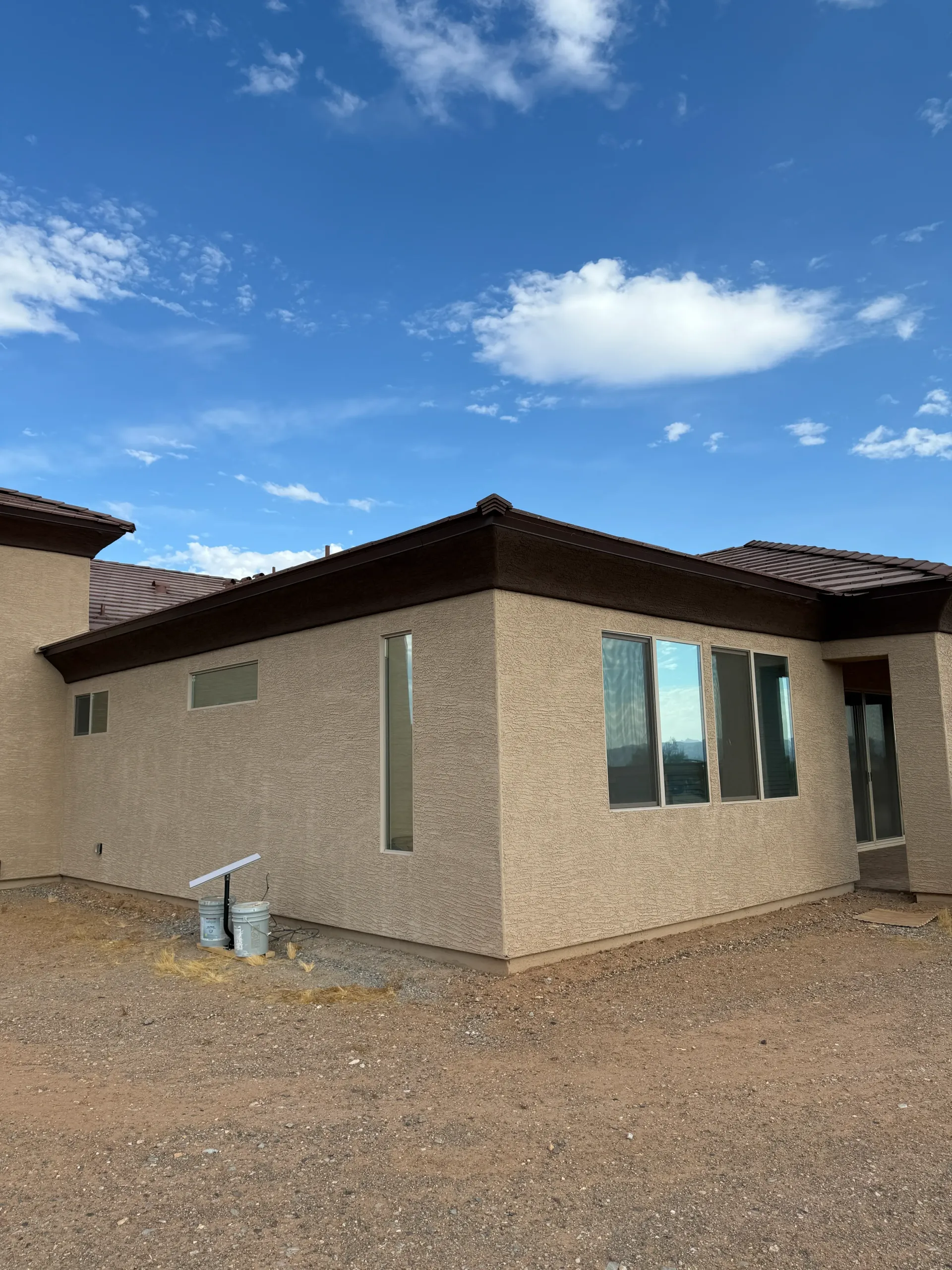 Beige stucco house with brown trim and roof against a blue sky.