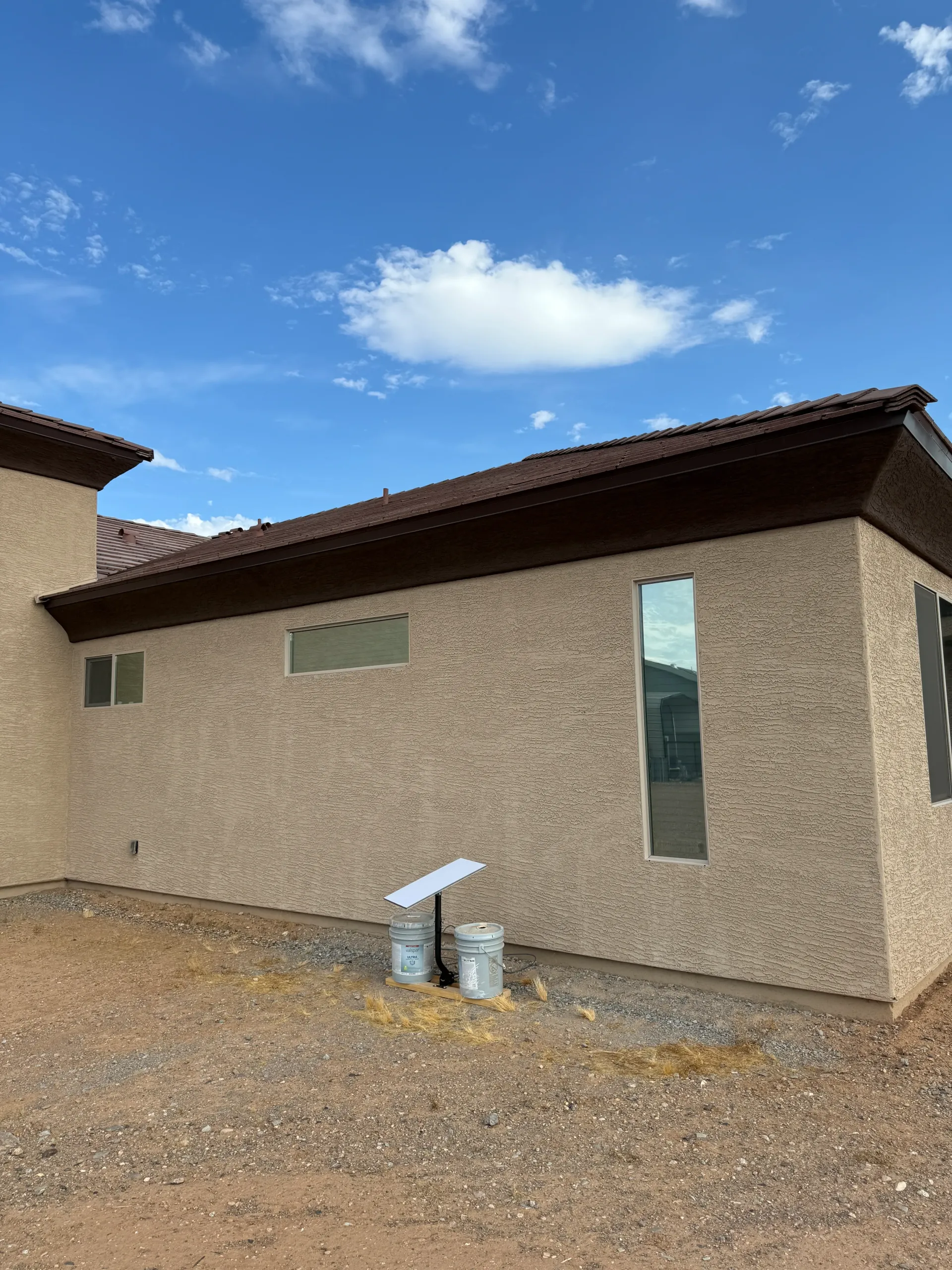 Beige stucco house with brown roof and narrow windows against a blue sky with clouds.
