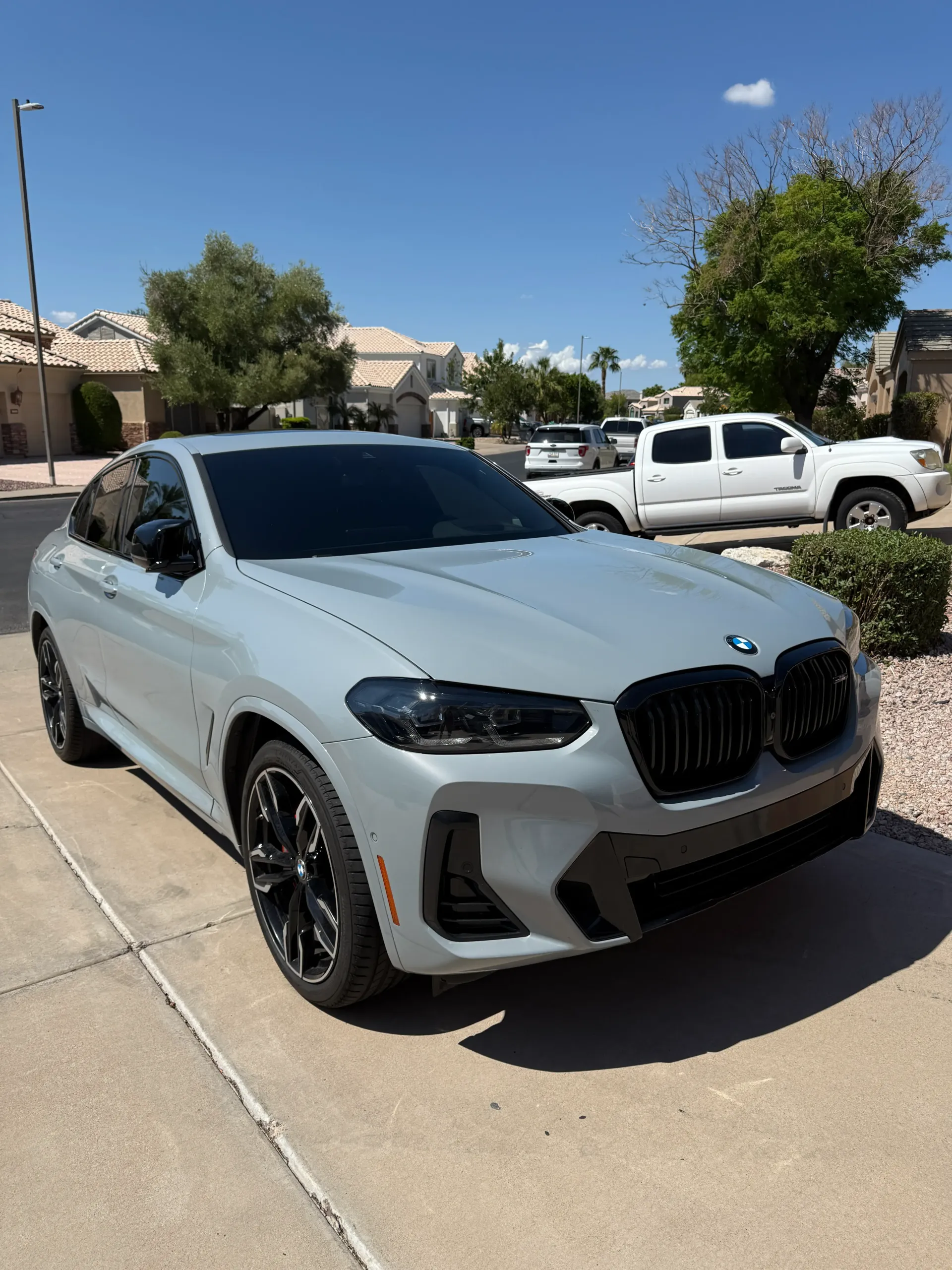 Gray BMW X4 parked on a driveway with black accents, under a clear blue sky.