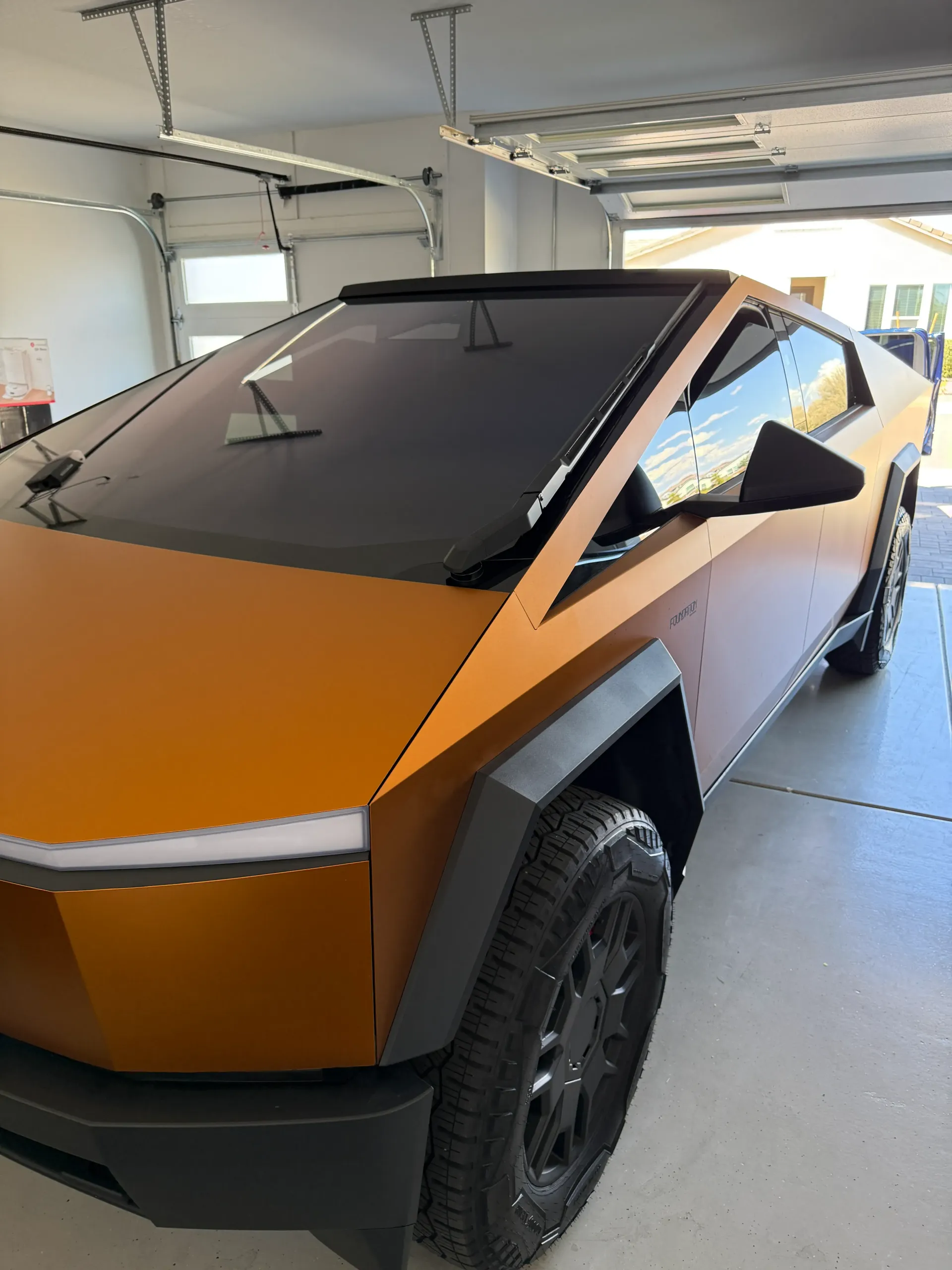 Tesla Cybertruck with orange wrap parked in a garage.
