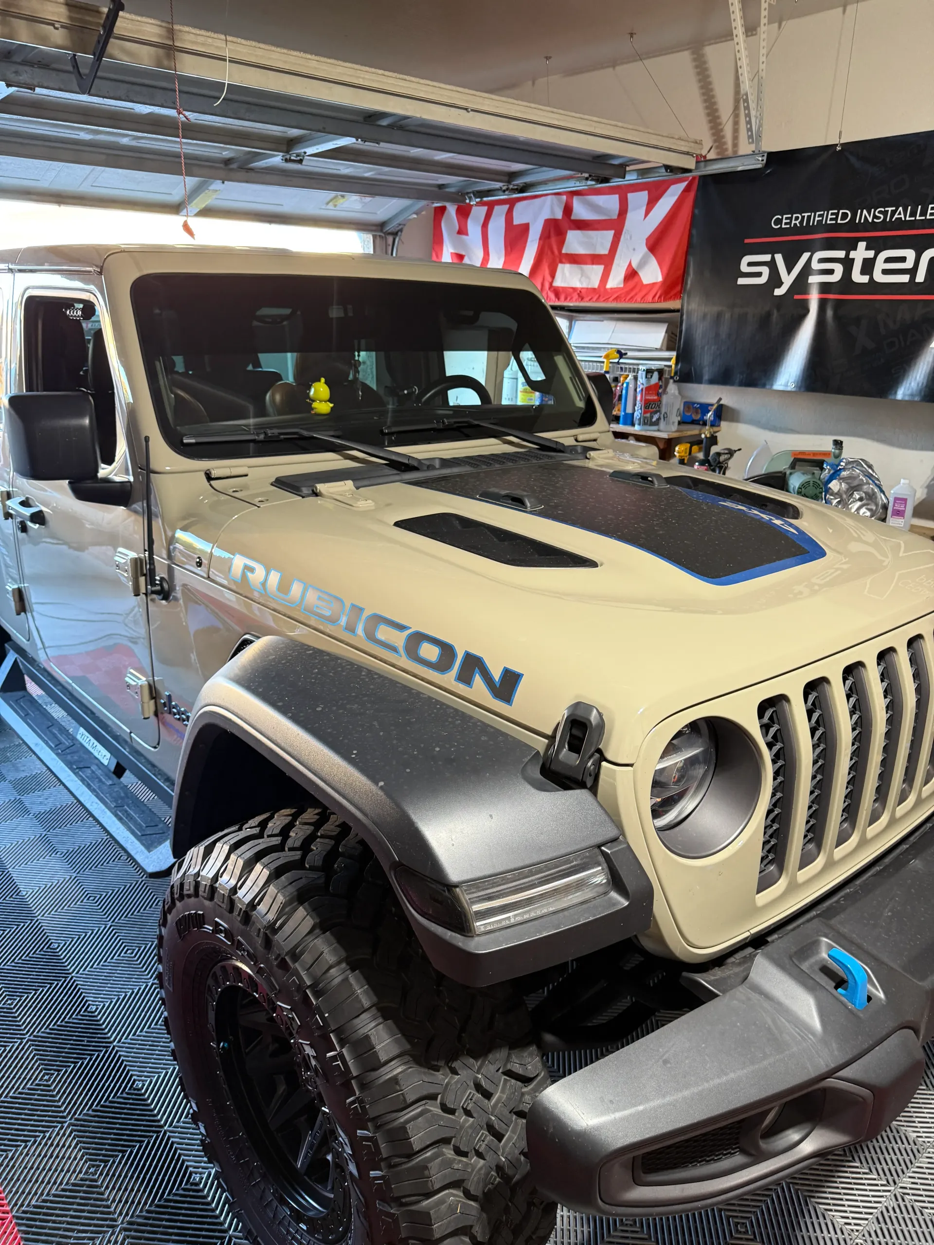 Tan Jeep Rubicon parked in a garage, black fender flares, and blue accents.