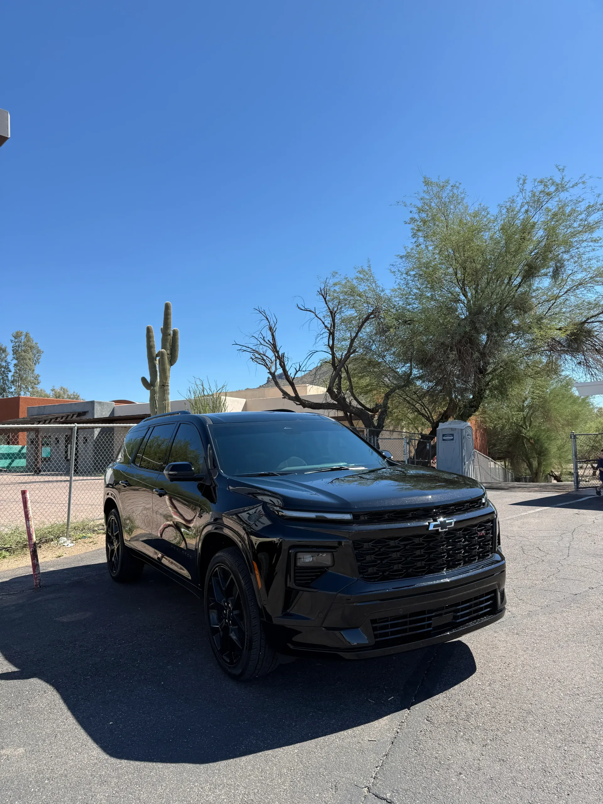 Black SUV parked outside on a sunny day with cactus and trees in background.