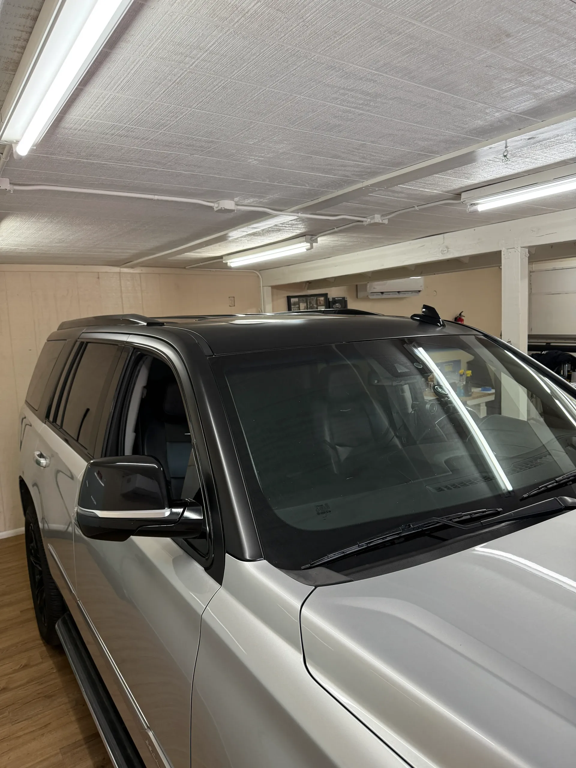 Silver SUV with black roof, in a garage with fluorescent lights.