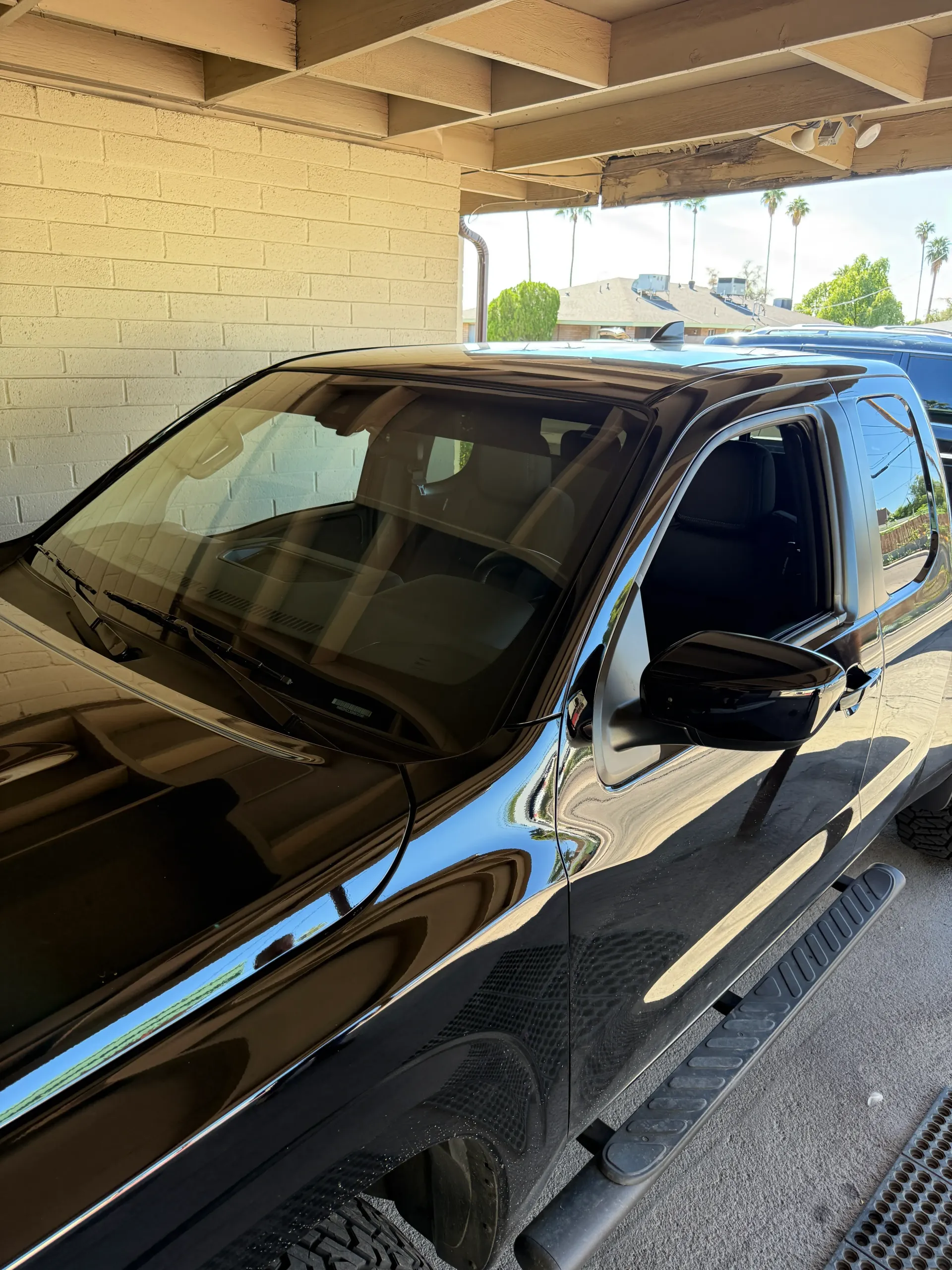 Black car parked under a beige overhang. Reflection of the sky in the windshield.