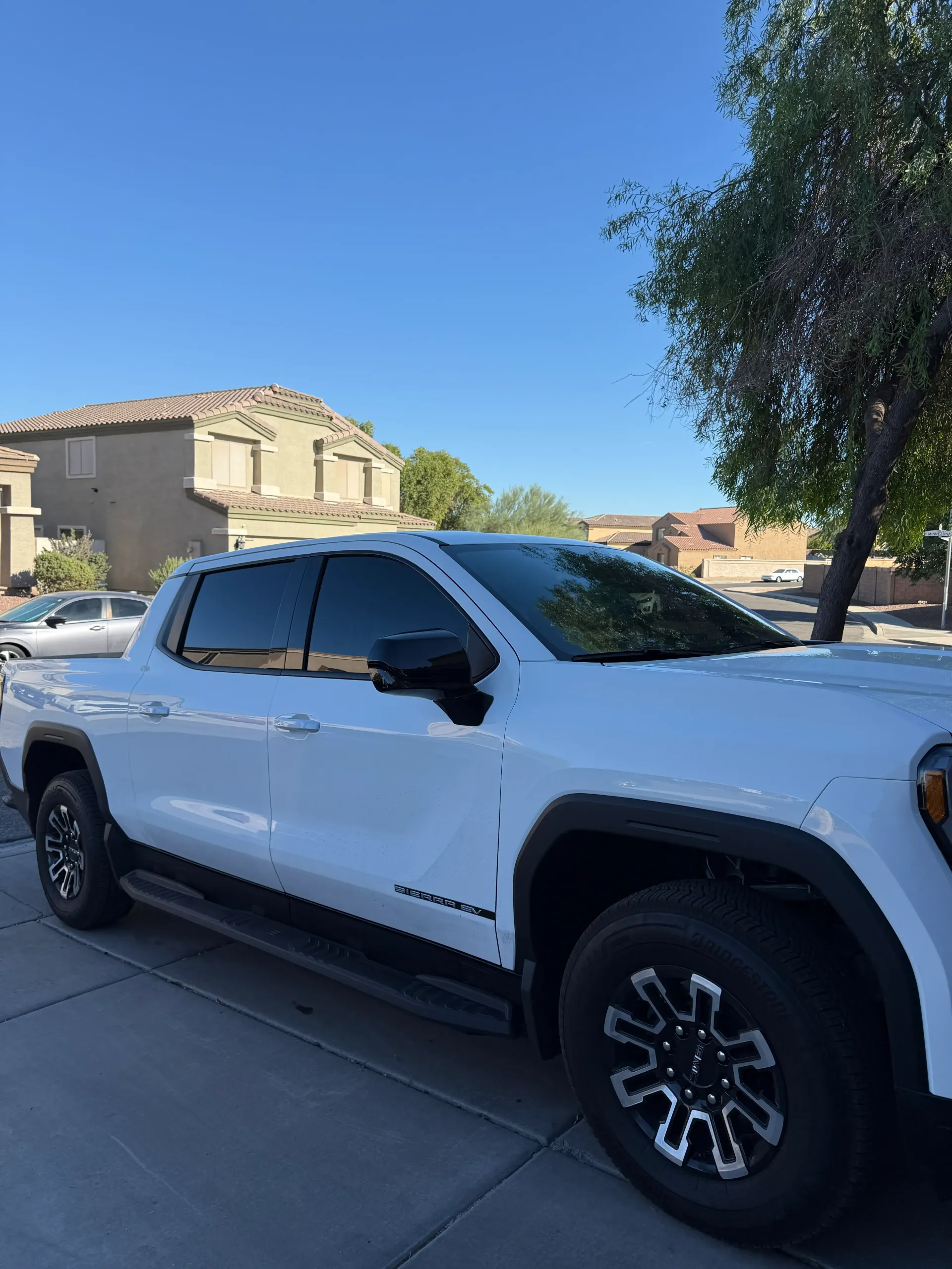 White GMC Sierra truck parked on a street in front of a house.