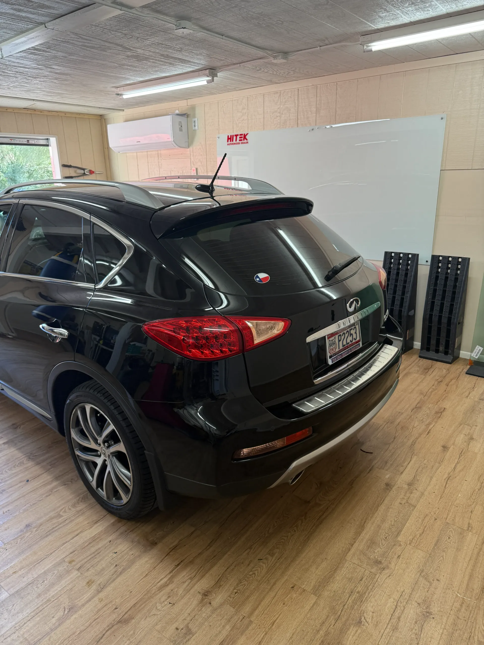 Black SUV parked in a garage; taillight visible, license plate and window tinting supplies nearby.