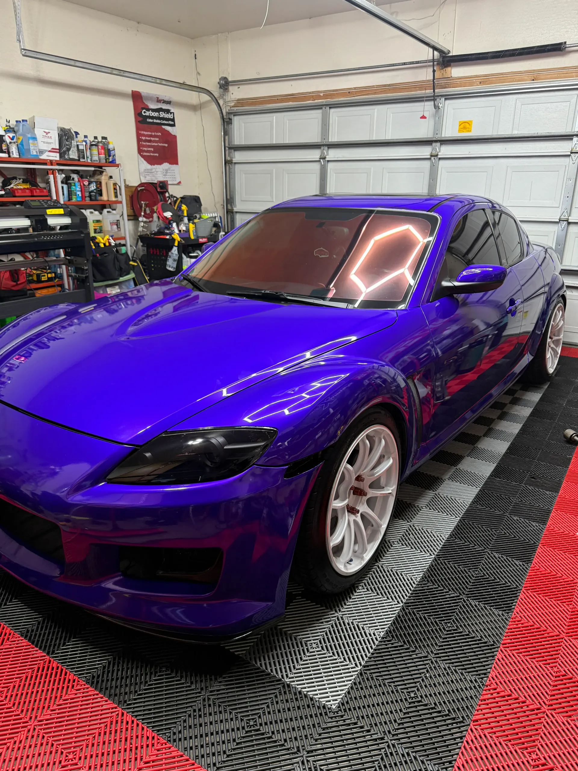 Purple sports car with tinted windows parked in a garage with tiled flooring.