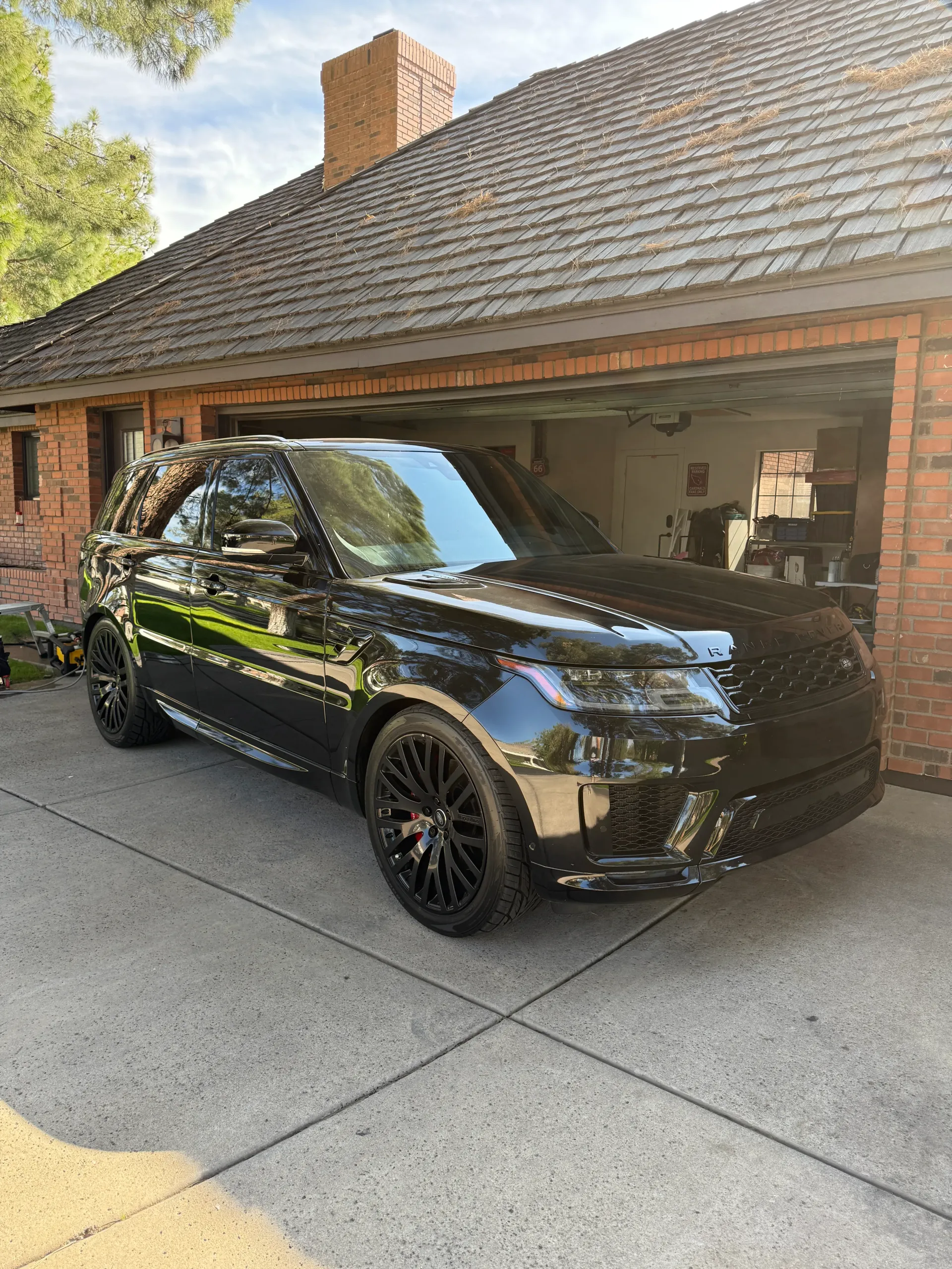 Black Range Rover parked in a driveway, in front of a brick house with a garage.