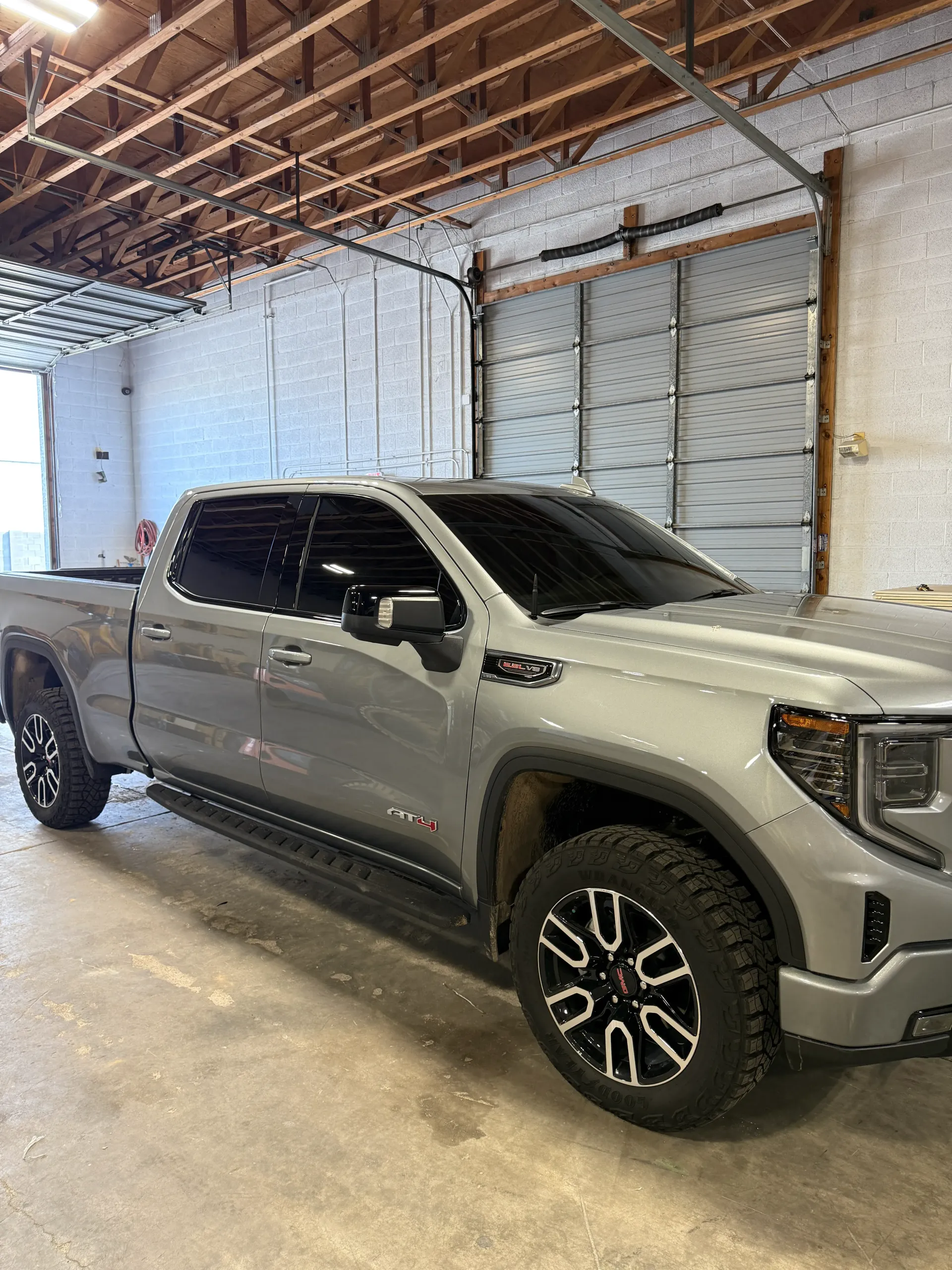 Gray GMC Sierra pickup truck parked inside a garage. Dark tinted windows and black and silver wheels.