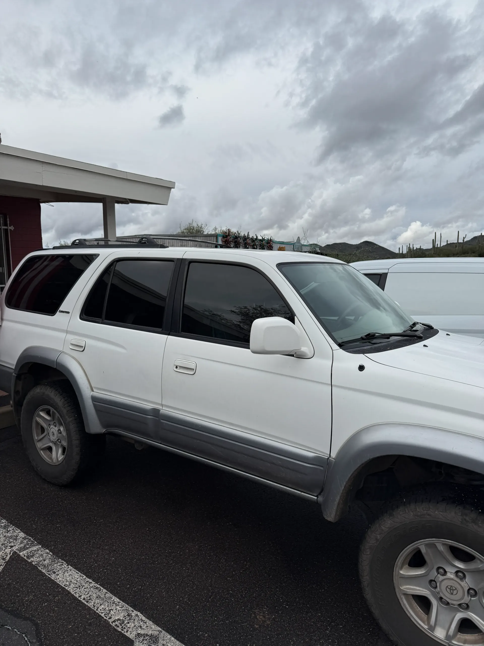 White SUV parked outside with dark tinted windows. Gray trim. Cloudy sky.