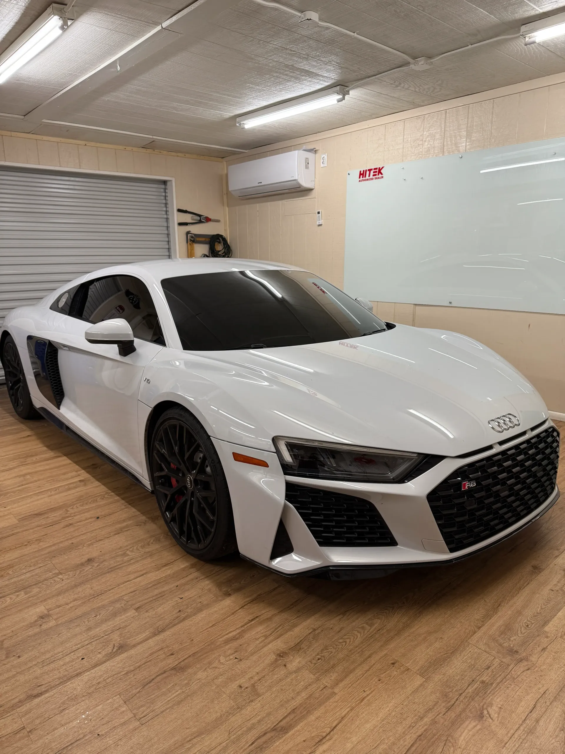 White Audi R8 sports car parked in a garage with a wooden floor.