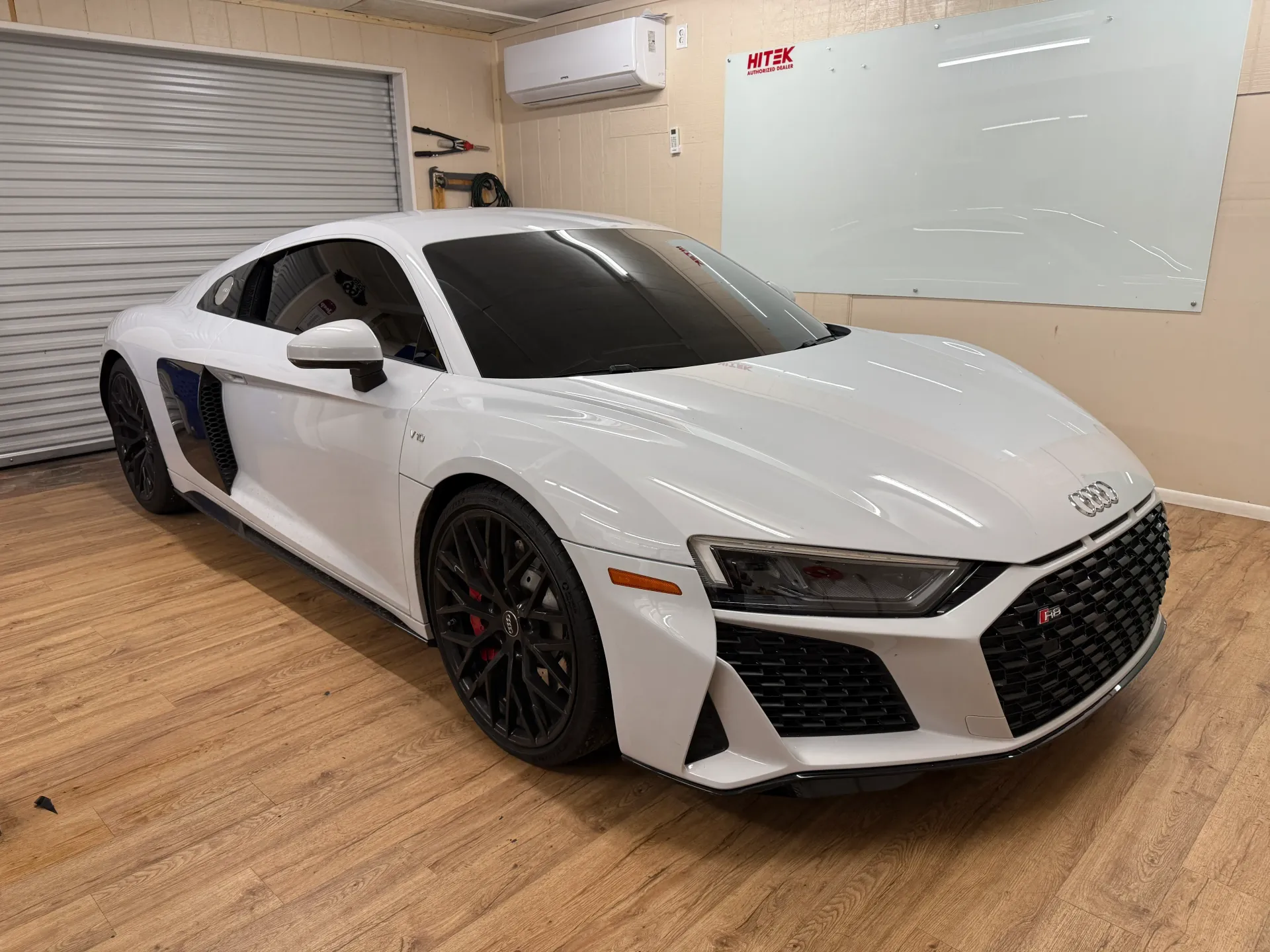 White Audi R8 sports car in a garage with tinted windows and black wheels.