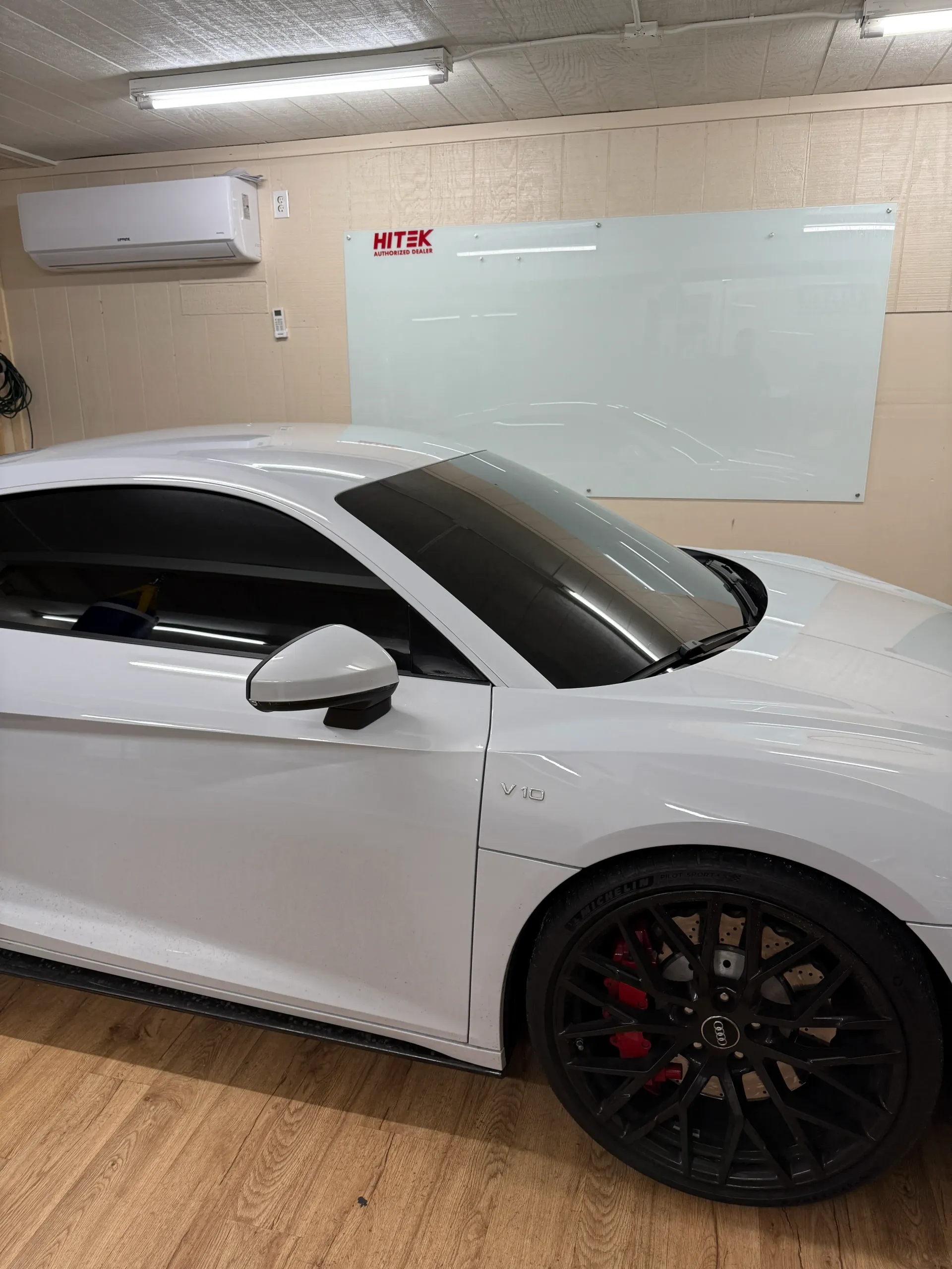 White sports car with black rims in a garage; red brake calipers.