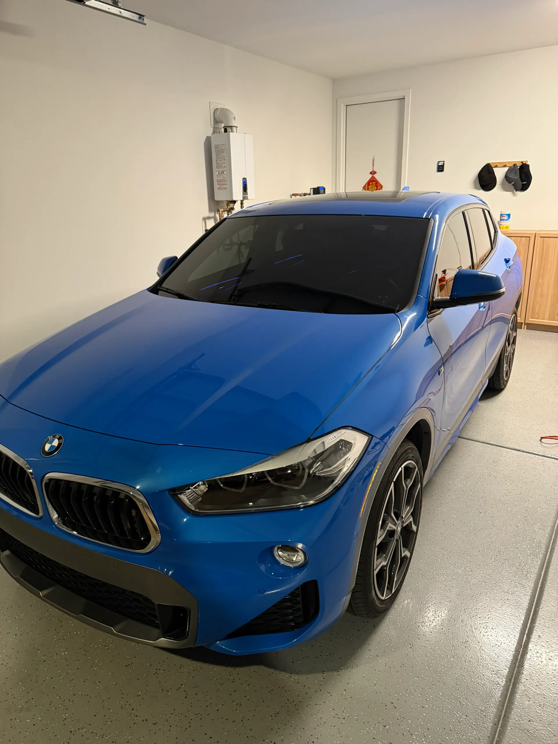 Blue BMW X2 parked in a garage with epoxy flooring and a tankless water heater.
