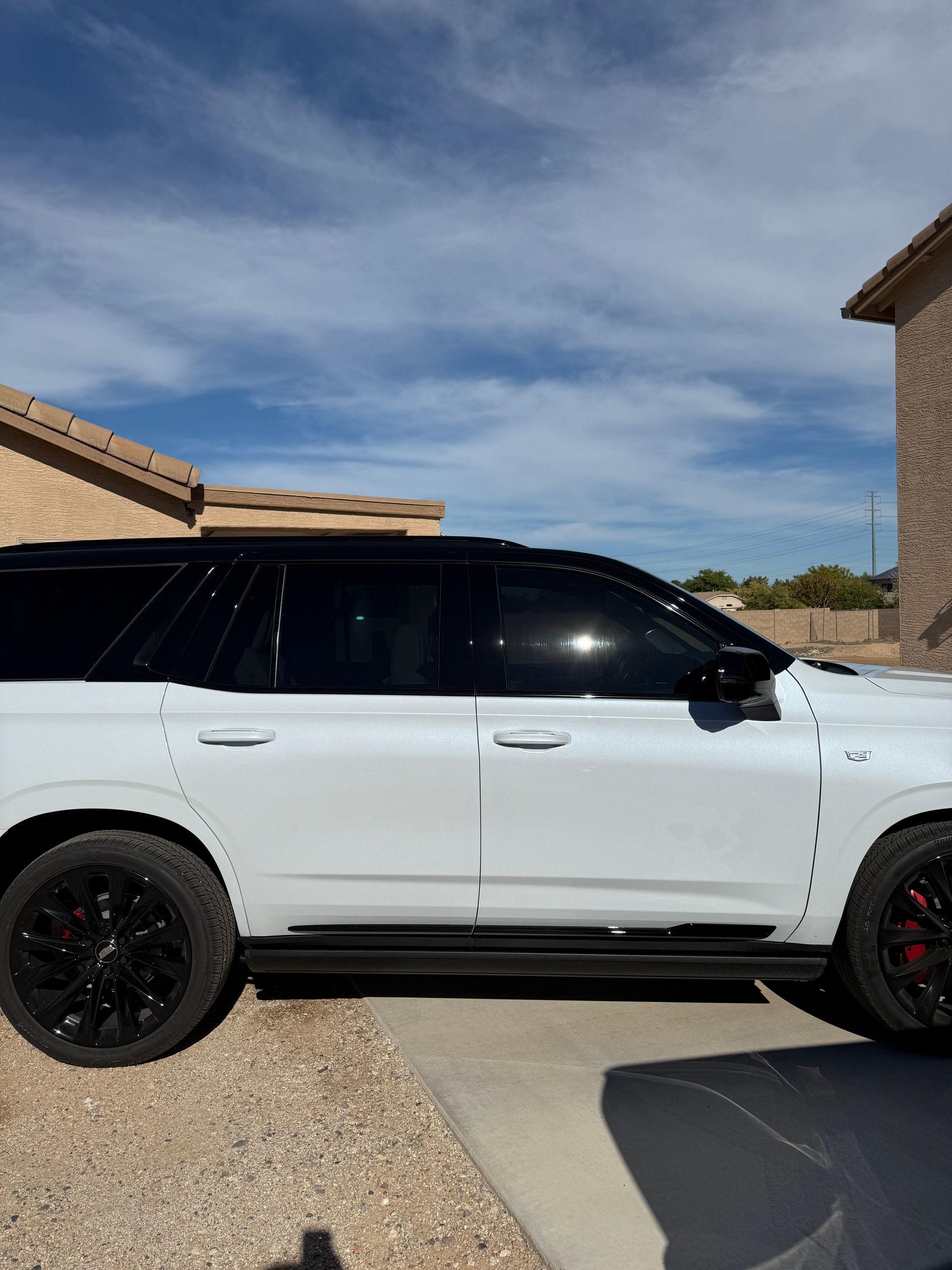 White SUV with black wheels and tinted windows parked outside a house on a sunny day.