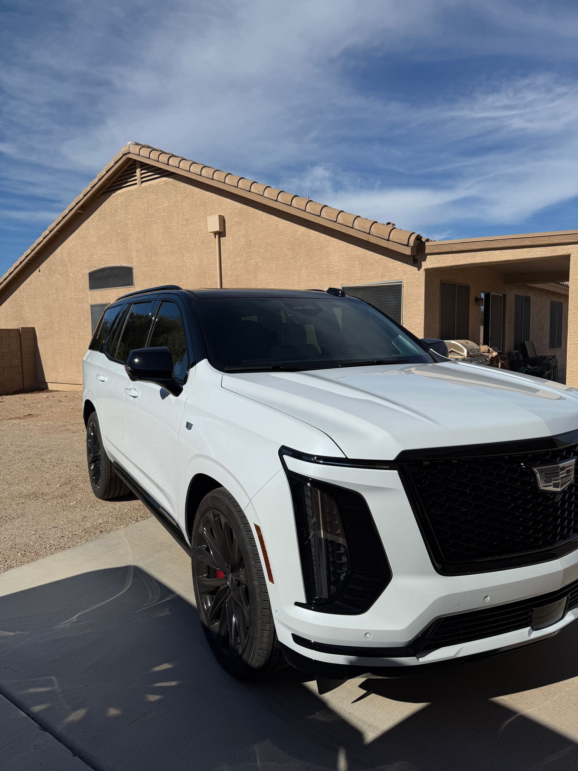 White Cadillac Escalade SUV parked in front of a beige house on a sunny day.