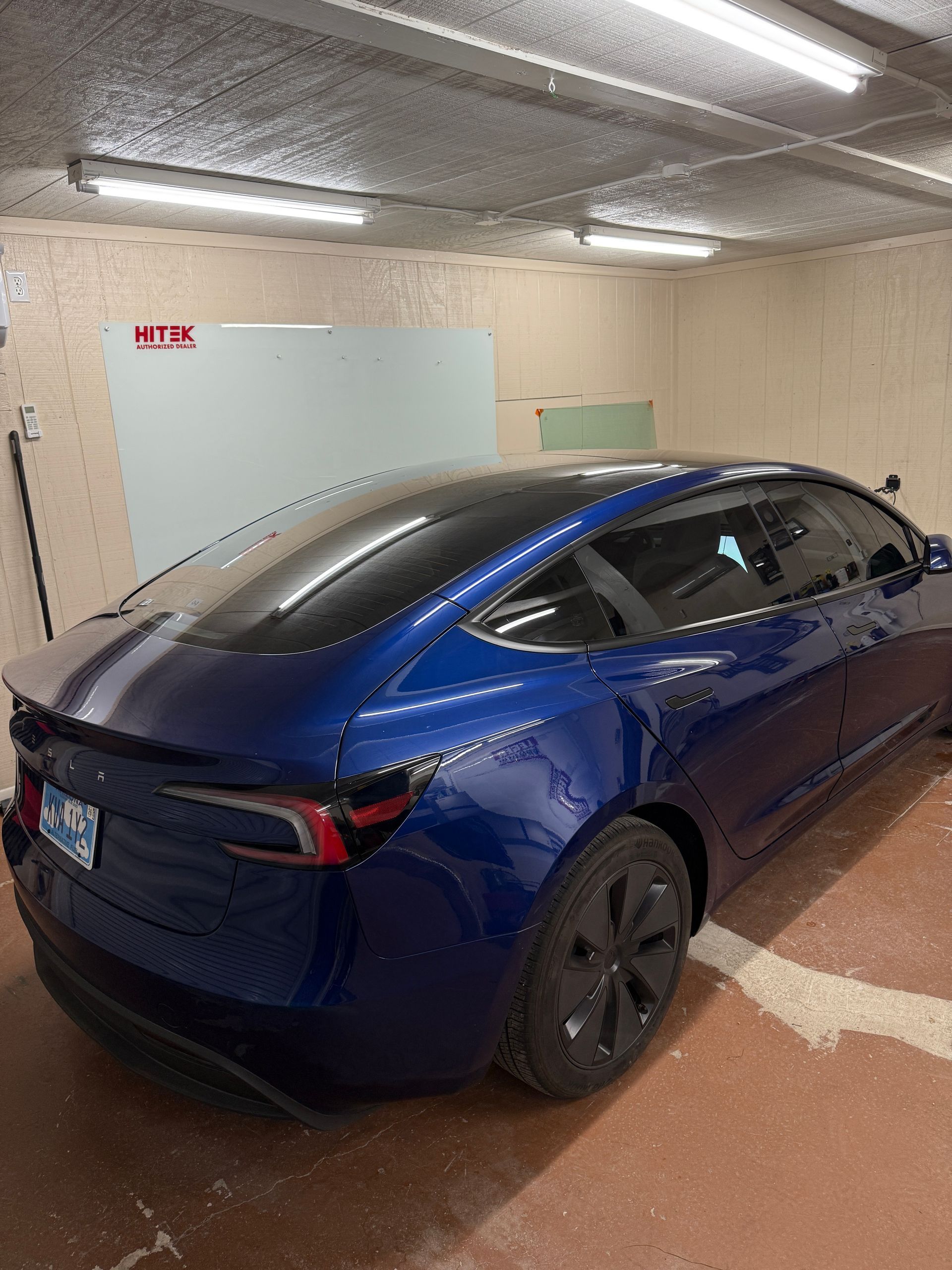 Blue Tesla parked in a garage with fluorescent lights.