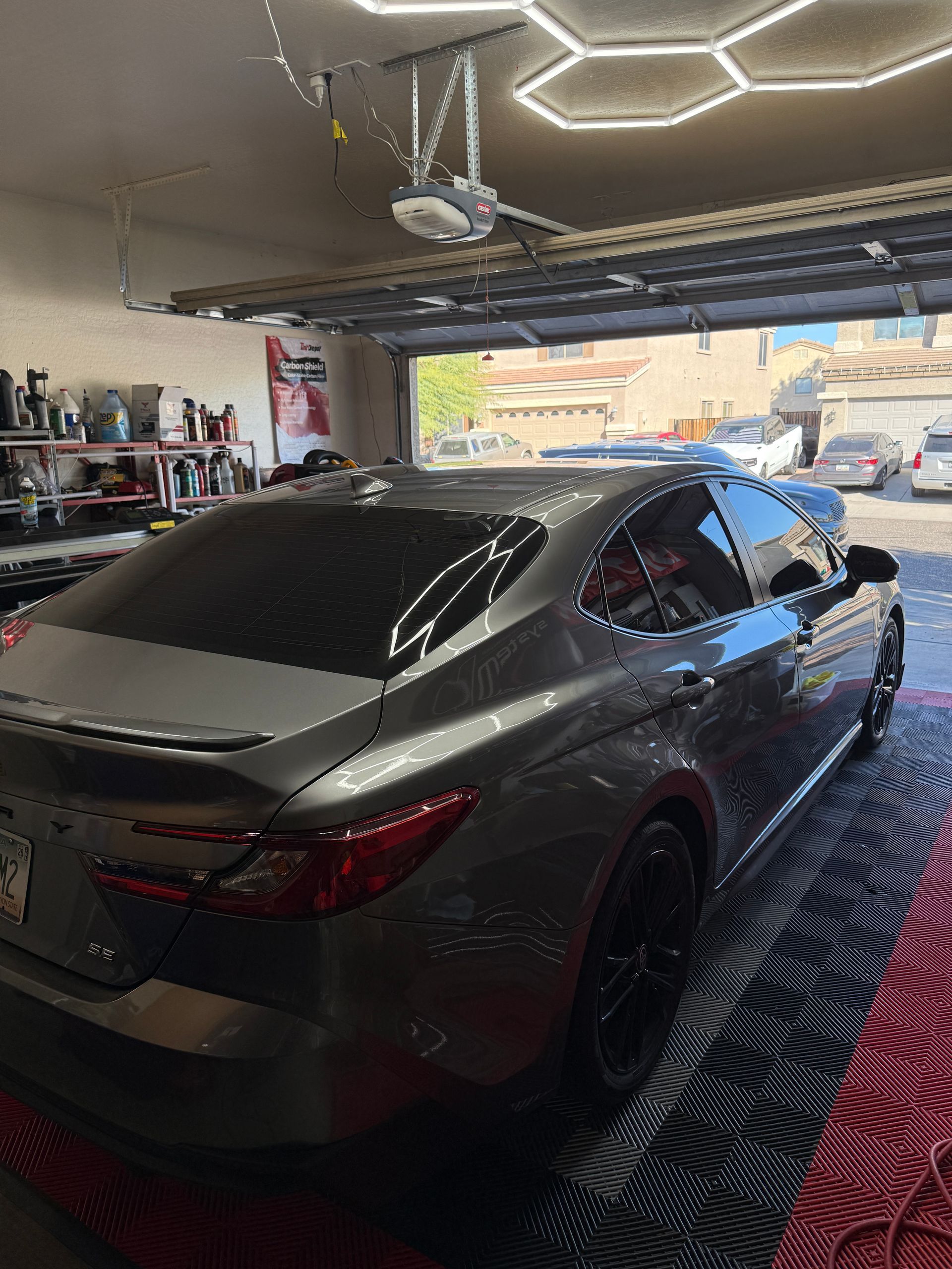 Gray sedan with tinted windows in a garage, under honeycomb lights.