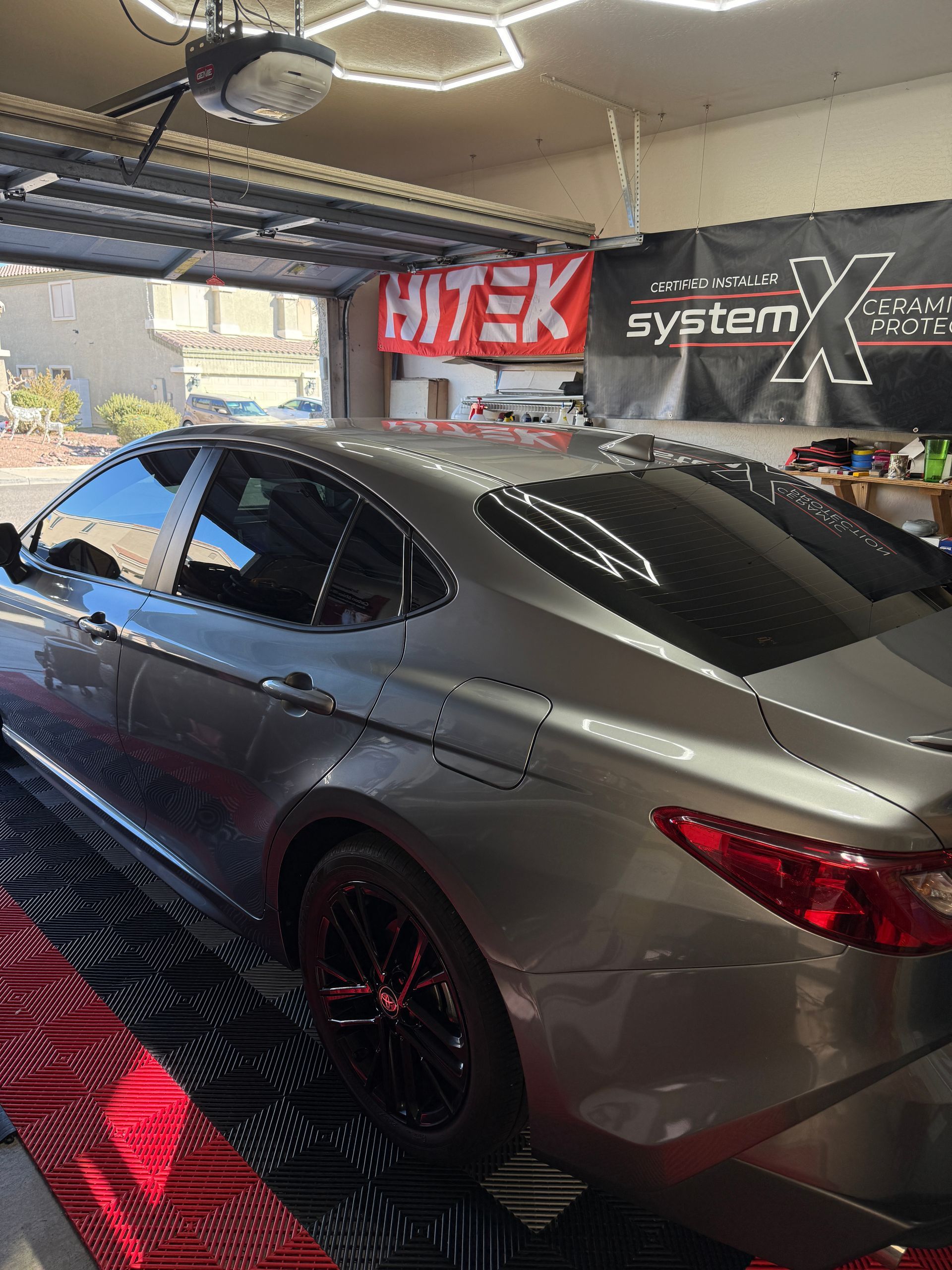 Gray sedan with tinted windows parked inside a garage. Red floor matting and banners are visible.