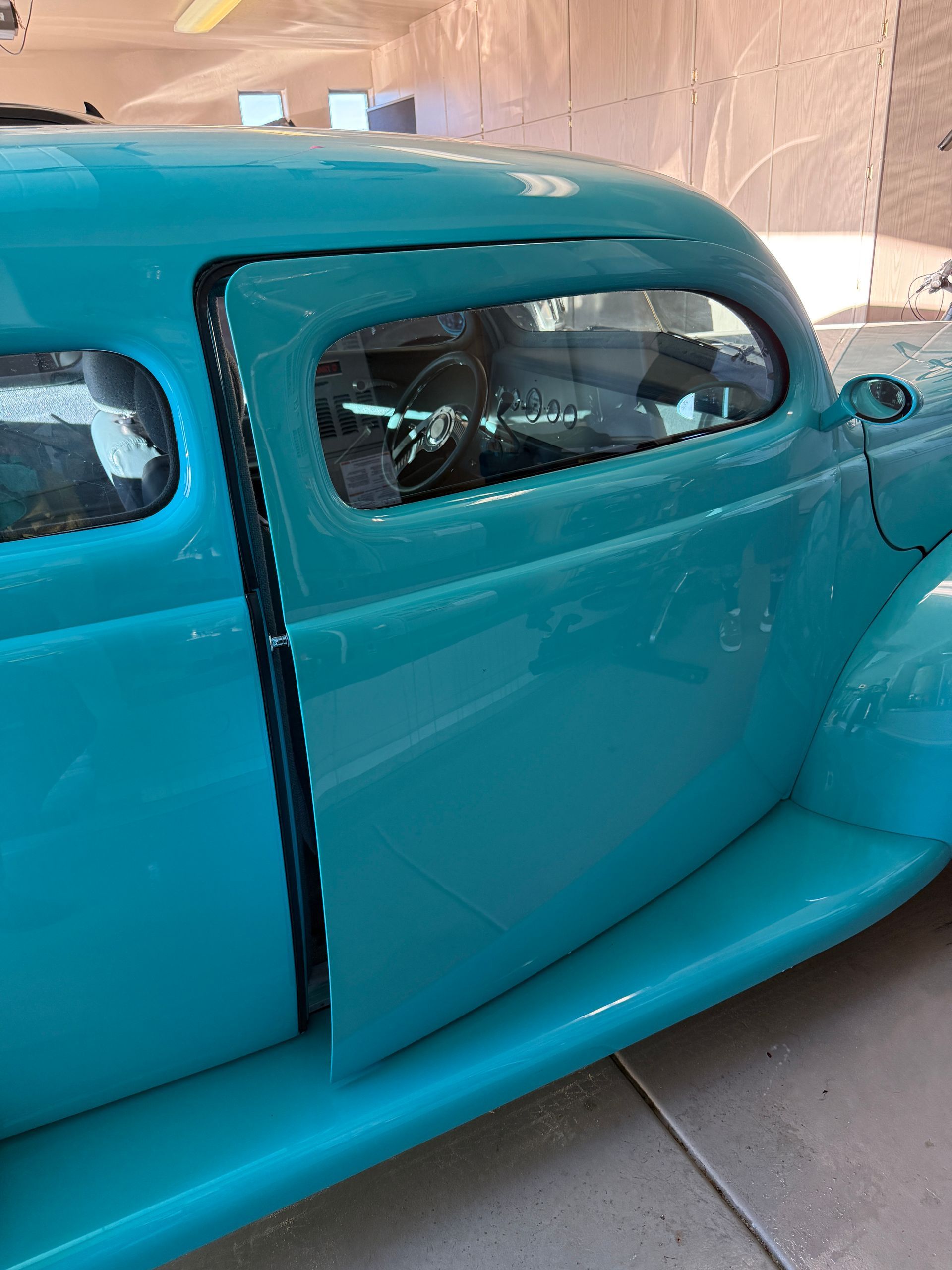 Teal-colored classic car with an open door, parked indoors.