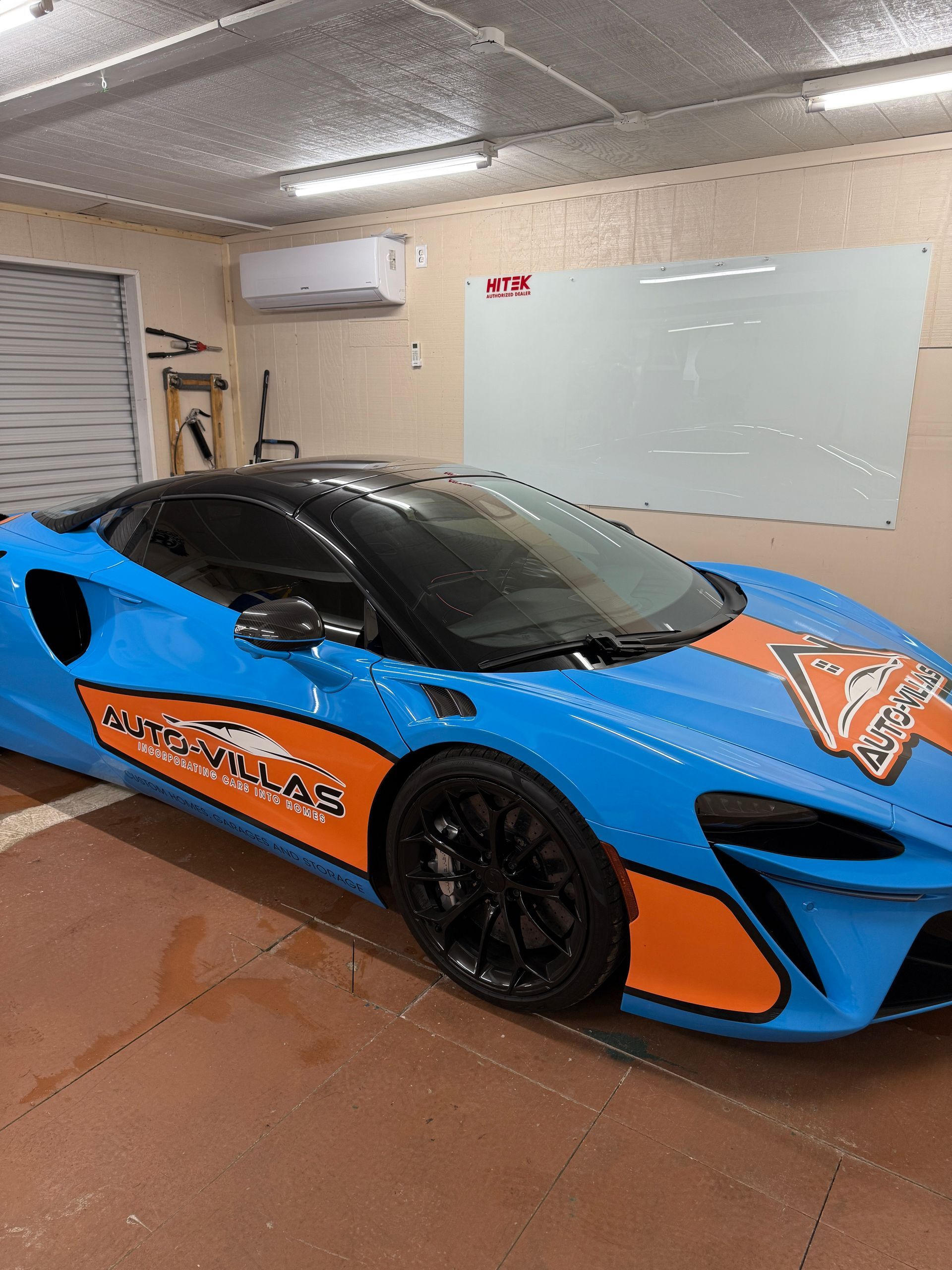 Blue and orange McLaren sports car in a garage with a black roof and wheels.