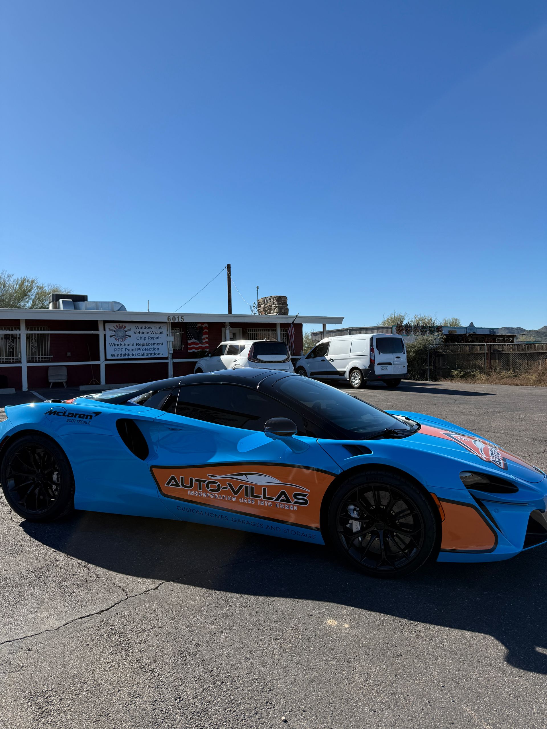 Blue and orange McLaren sports car parked in front of a building on a sunny day.