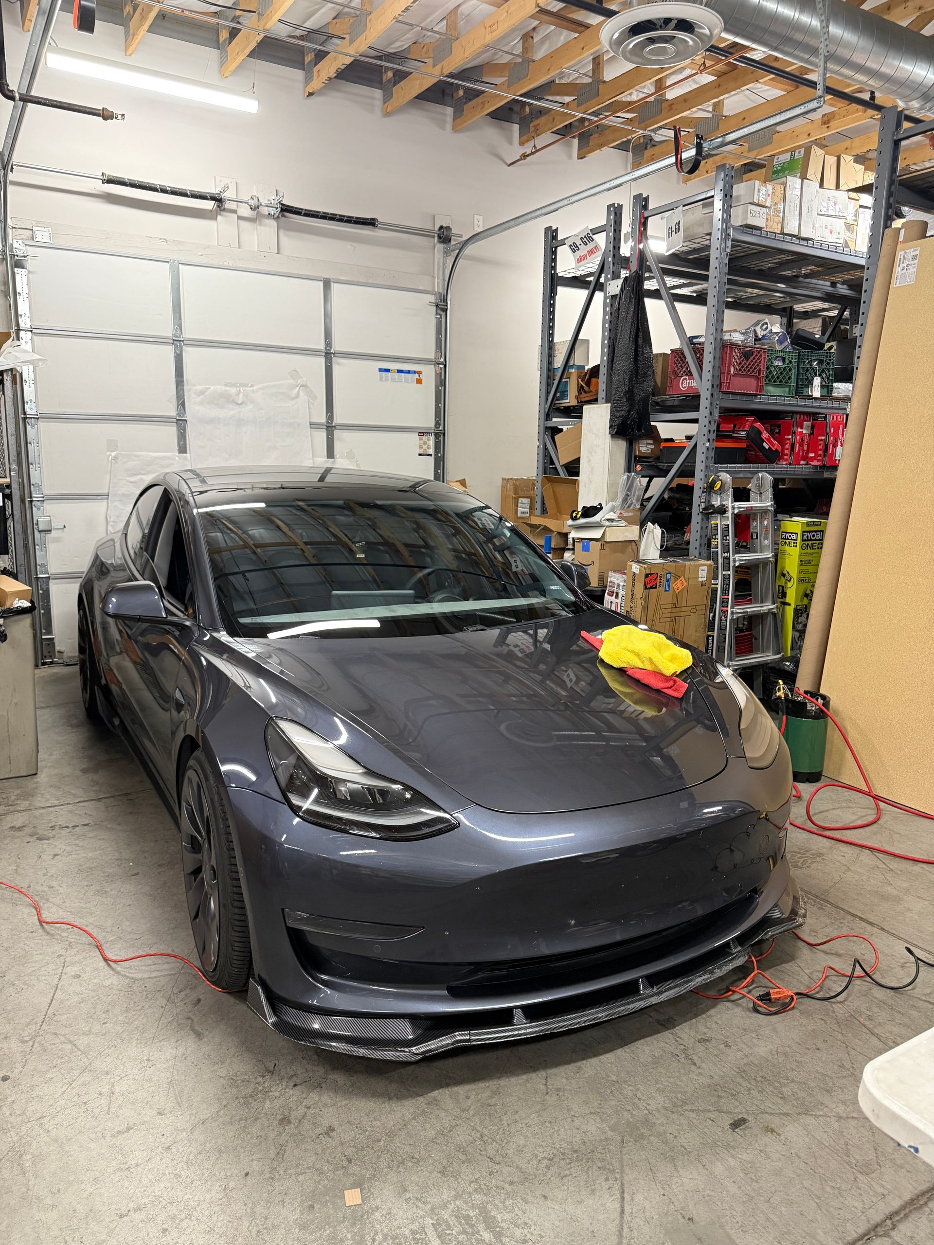 Gray Tesla Model 3 in a garage, with a front spoiler and a rag on the hood.