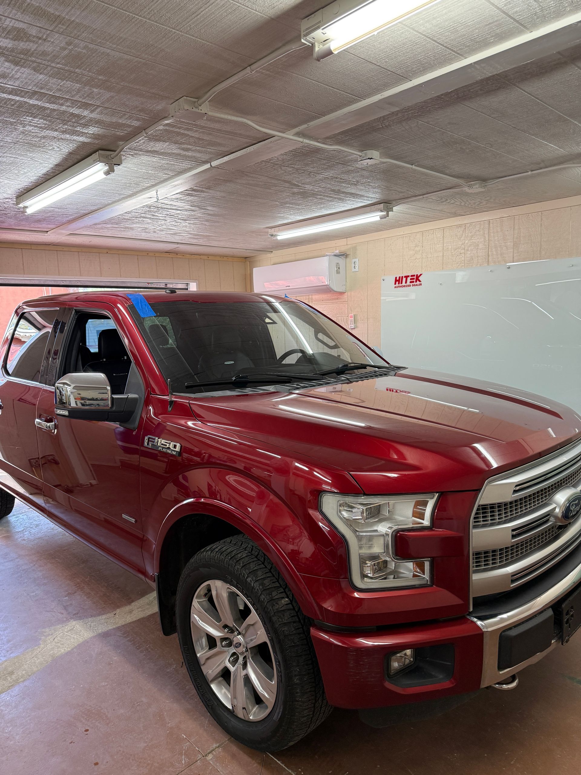 Red Ford F-150 truck parked in a garage with overhead lighting.