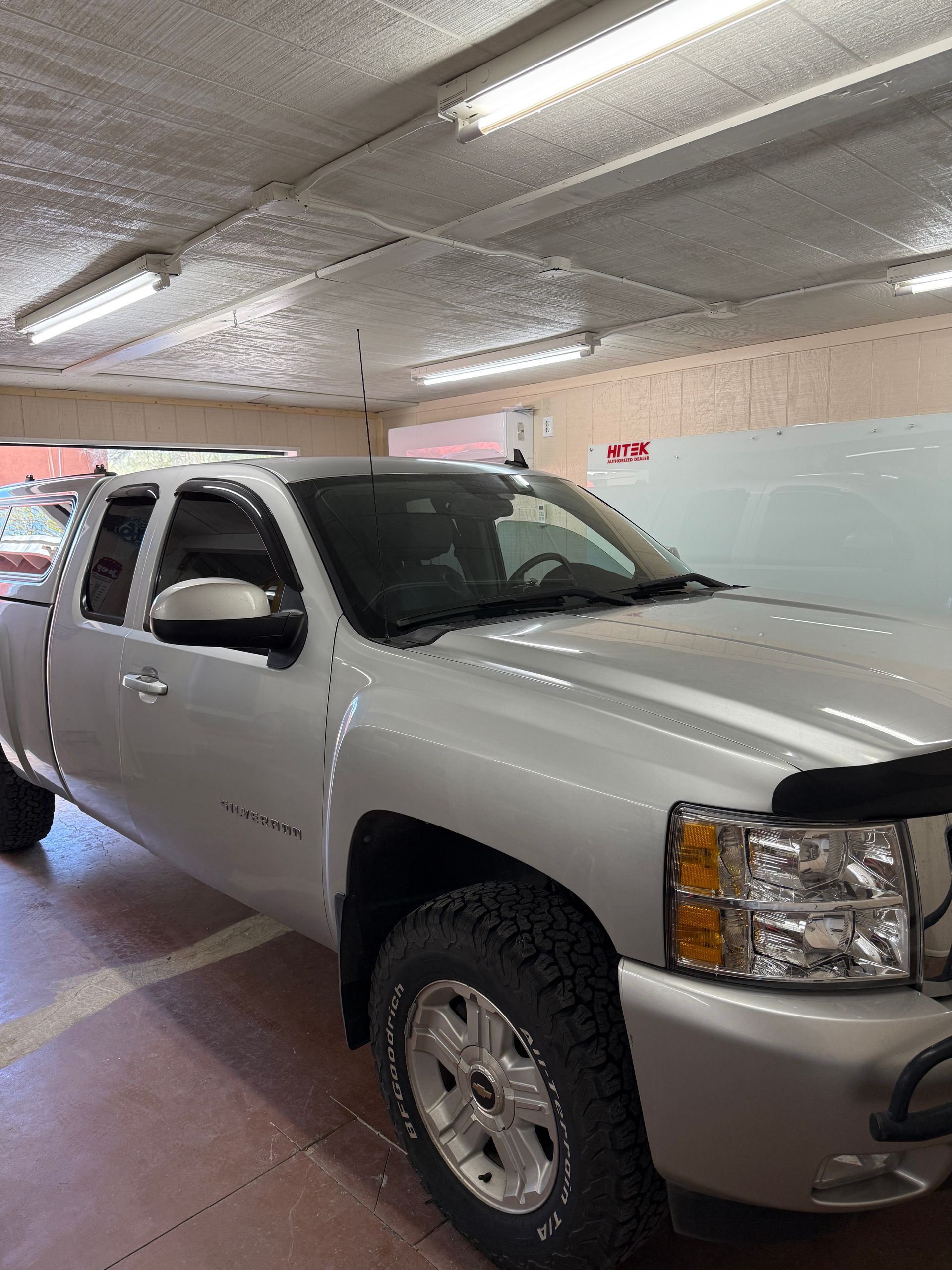 Silver Chevrolet pickup truck parked in a garage with fluorescent lights.