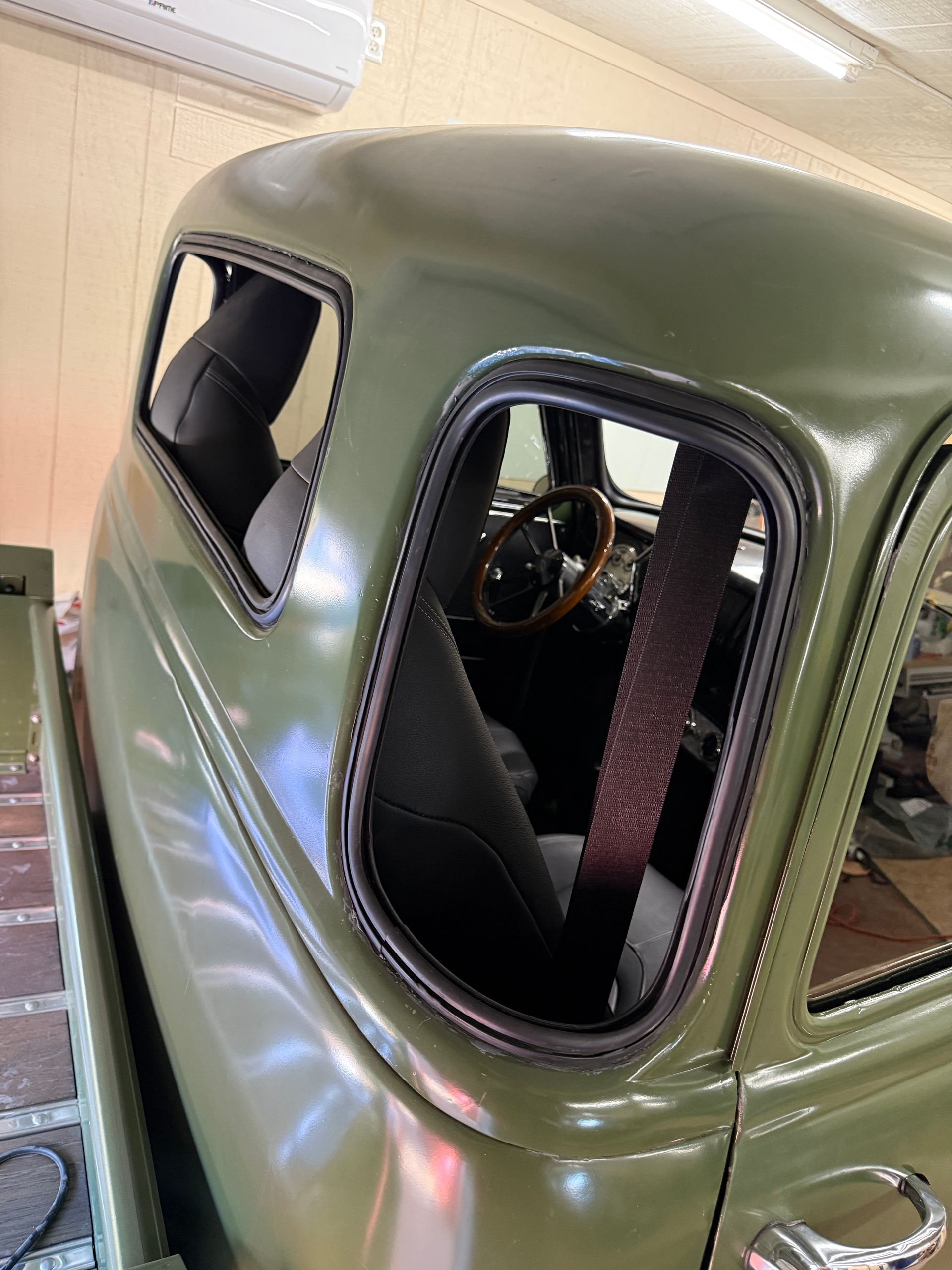 Green classic truck cab, side view showing windows, seats, and steering wheel.