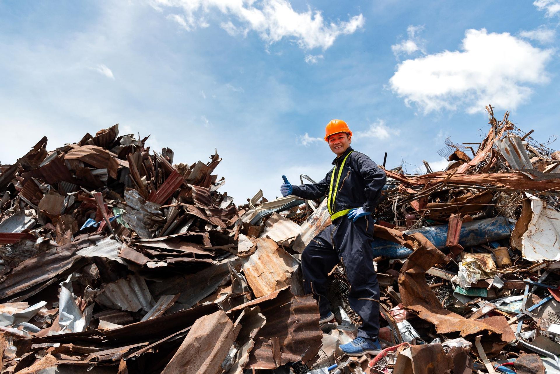 A man in a hard hat is standing in a pile of scrap metal.