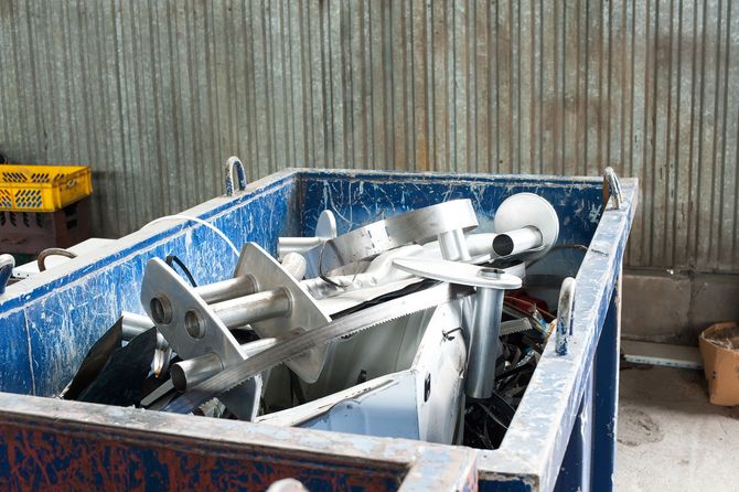 A blue dumpster filled with a lot of metal objects.