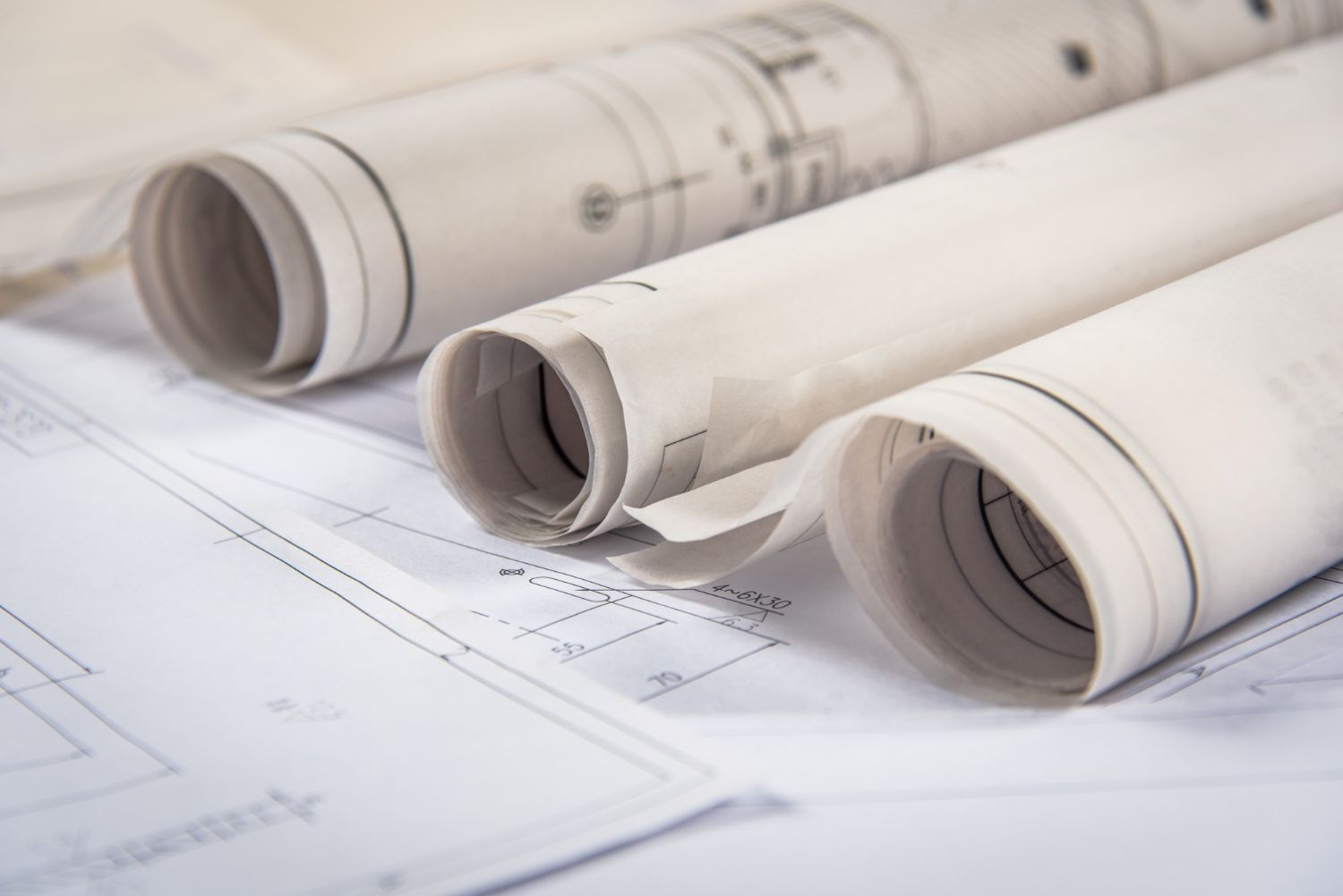 Primer plano de tres rollos de planos arquitectónicos que descansan sobre un dibujo técnico desenrollado.