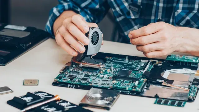 technician installing laptop fan in a open laptop. laptop component parts are on work desk with repair tool