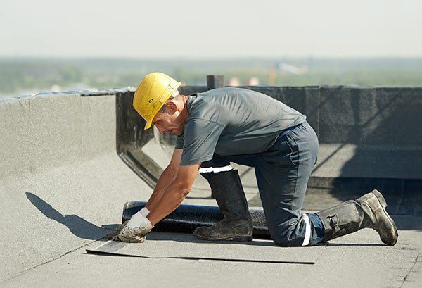 Un homme portant un casque de sécurité est agenouillé sur un toit.