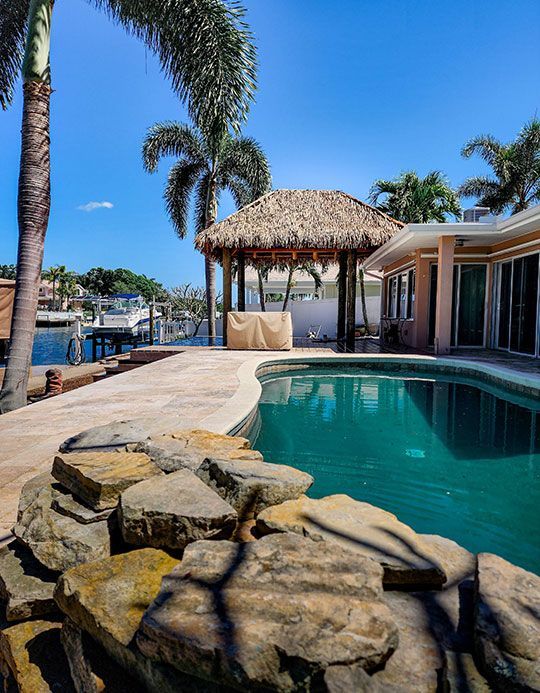 Swimming pool beside a waterway, thatched-roof gazebo, palm trees under a blue sky. Swimming pool beside a waterway, thatched-roof gazebo, palm trees under a blue sky.