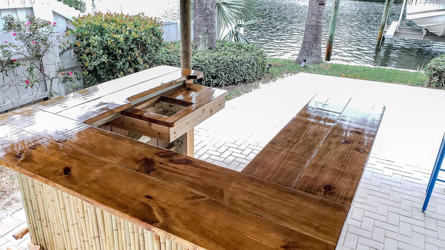 Outdoor wooden bar with thatched front, surrounded by a patio and greenery.
