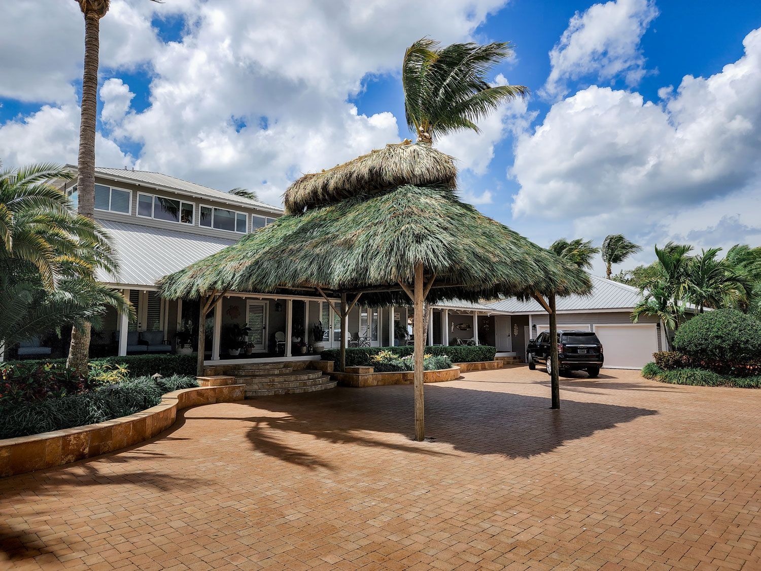 Beachfront home with thatched roof over driveway; car parked, blue sky.