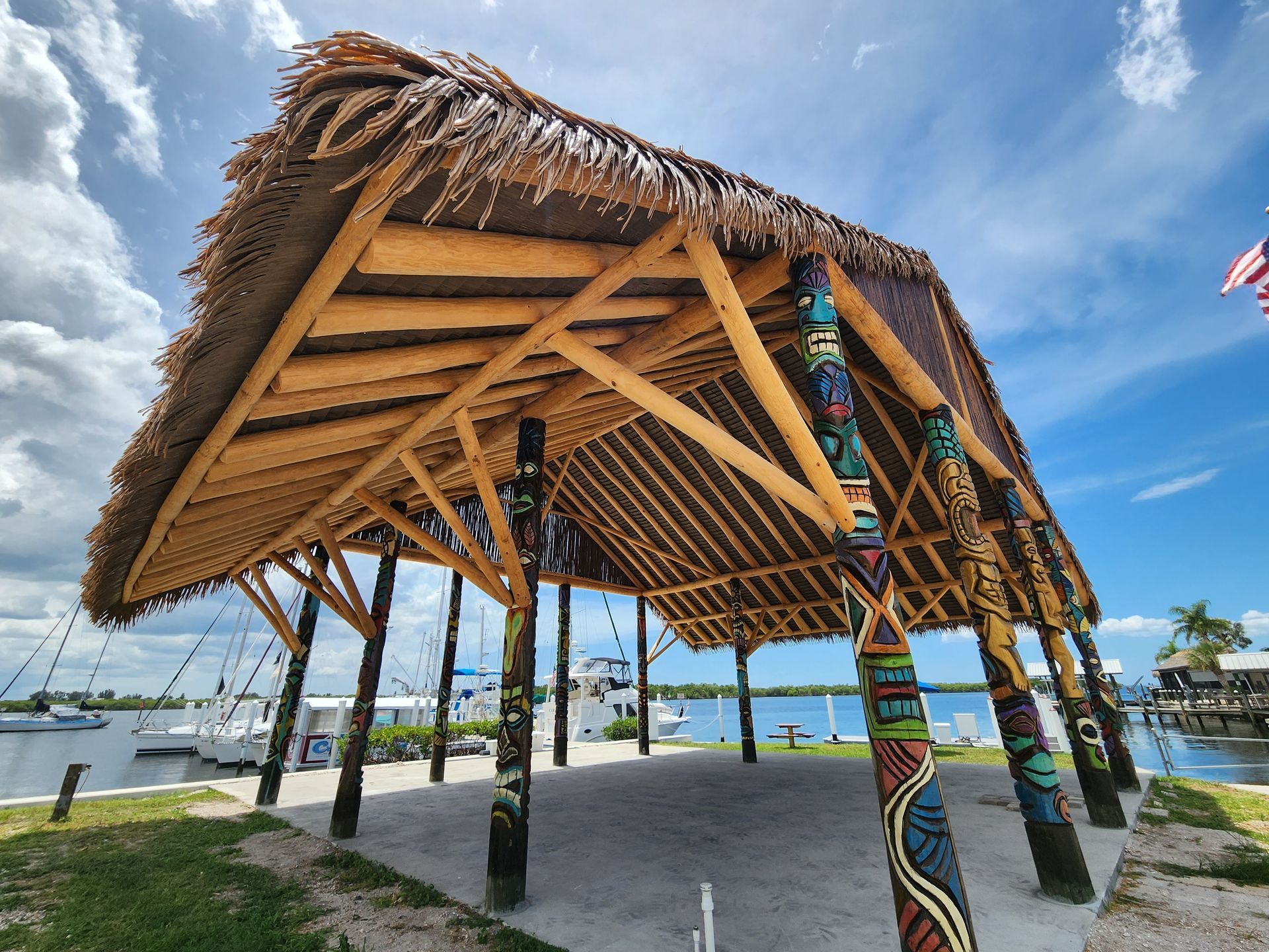 Gazebo with thatched roof, near a pool, with a building in the background. Sunny day.