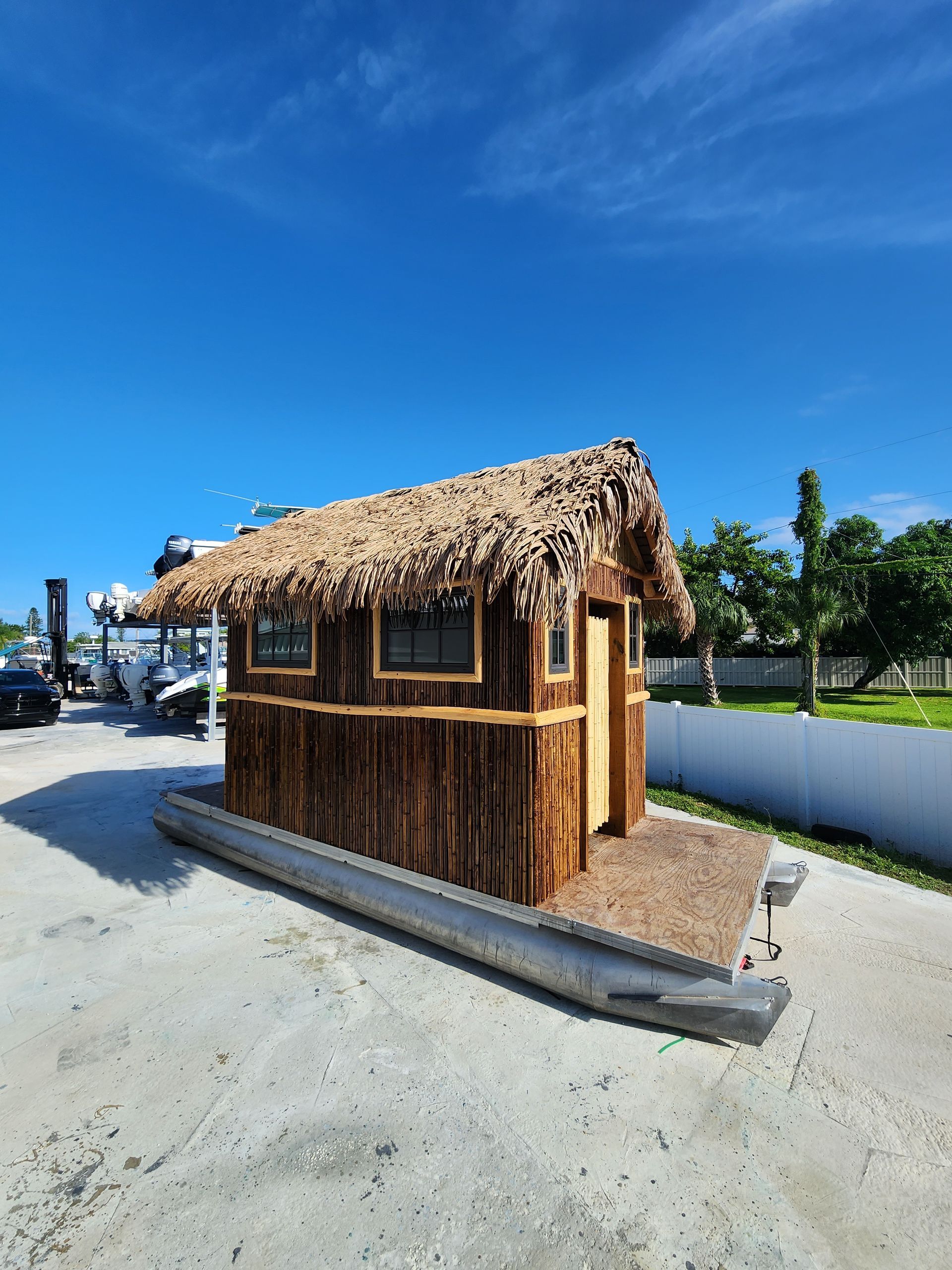 A small rustic cabin with a thatched roof sits on a pontoon, under a bright blue sky.