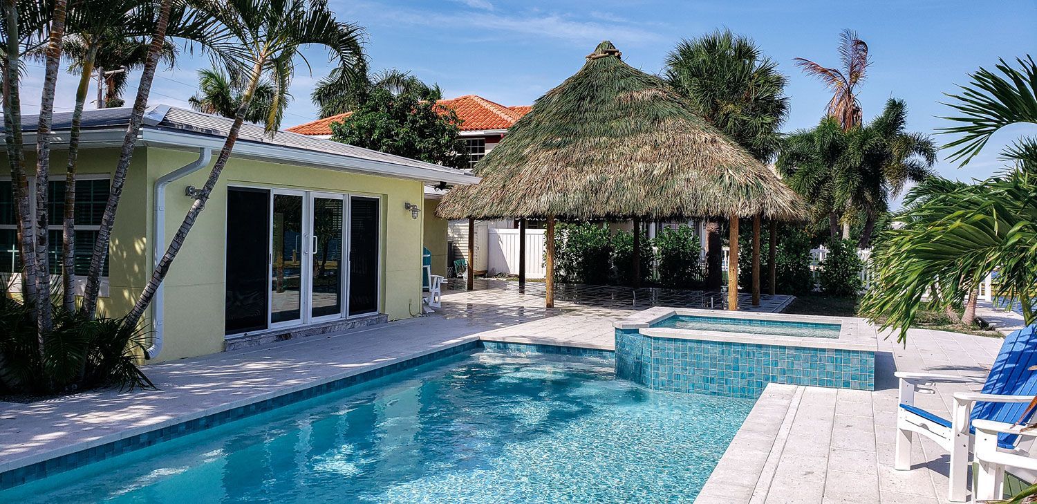 Swimming pool and hot tub with a thatch-roofed cabana and a light yellow building.