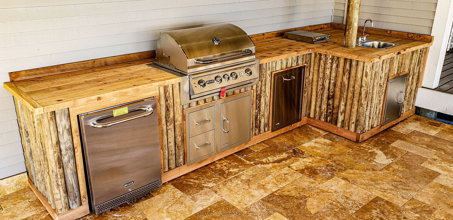 Outdoor kitchen with stainless steel appliances and wood paneling.