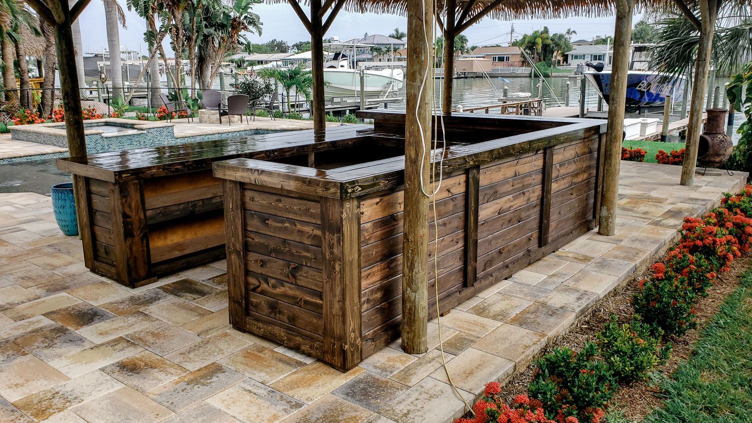 Outdoor wooden bar with thatched roof, on stone patio.