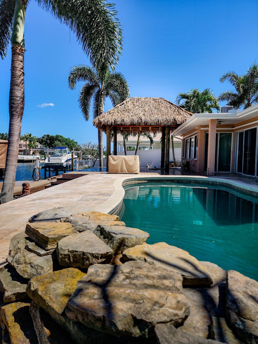 Poolside view with gazebo, palm trees, and waterfront. Clear blue sky, sunny day.