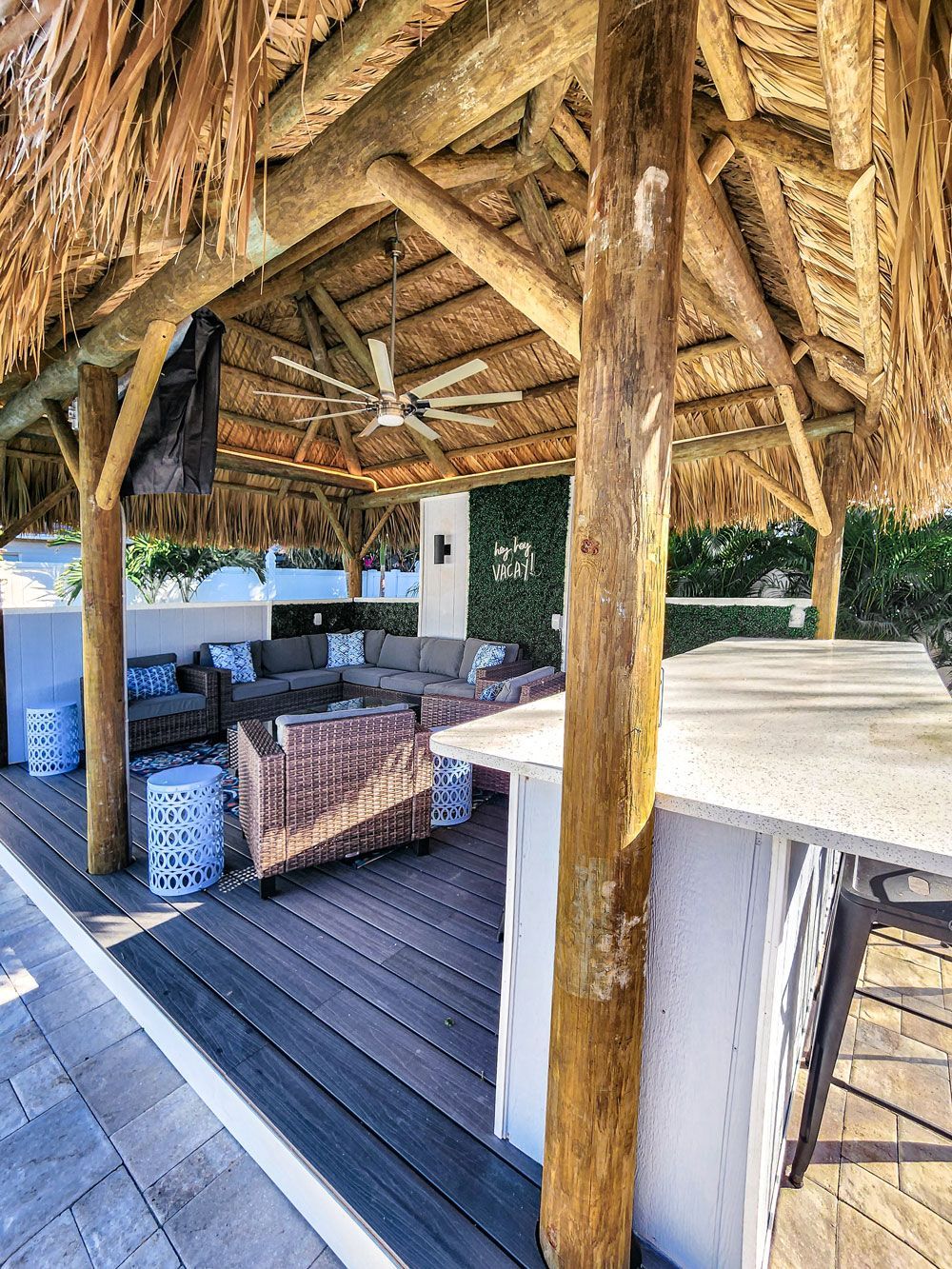 Tiki hut with a bar, seating area, ceiling fan, and wooden deck.