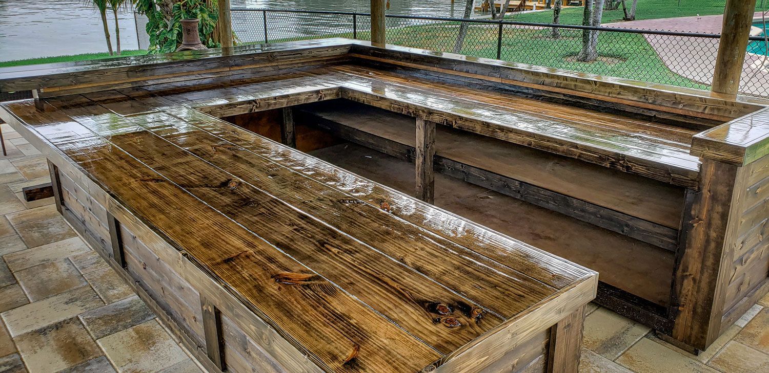 L-shaped wooden bar with wet, glossy surface and a stone tile floor.