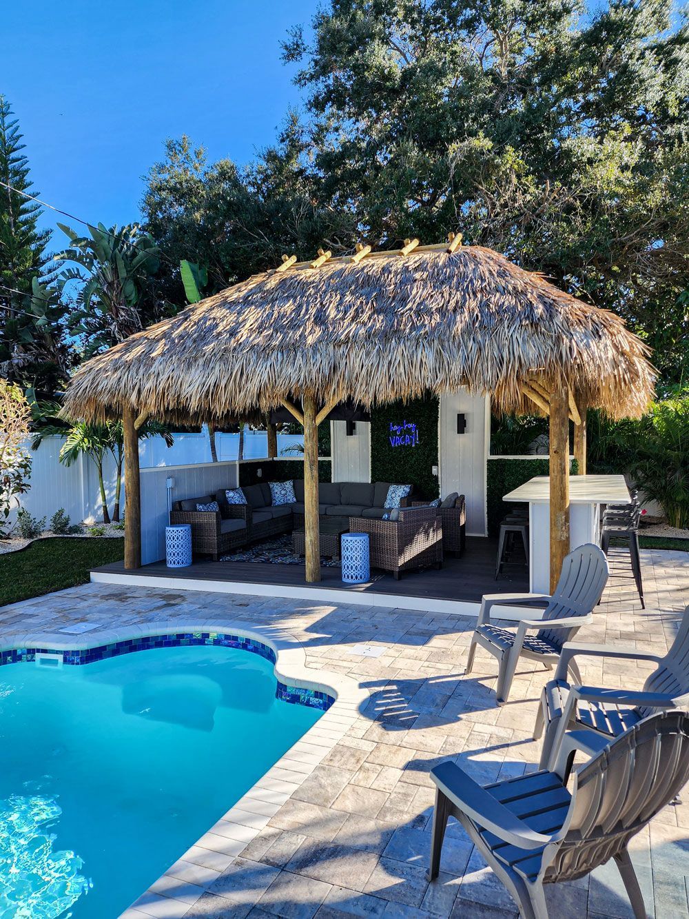 Tiki-style outdoor cabana with seating by a pool on a sunny day.