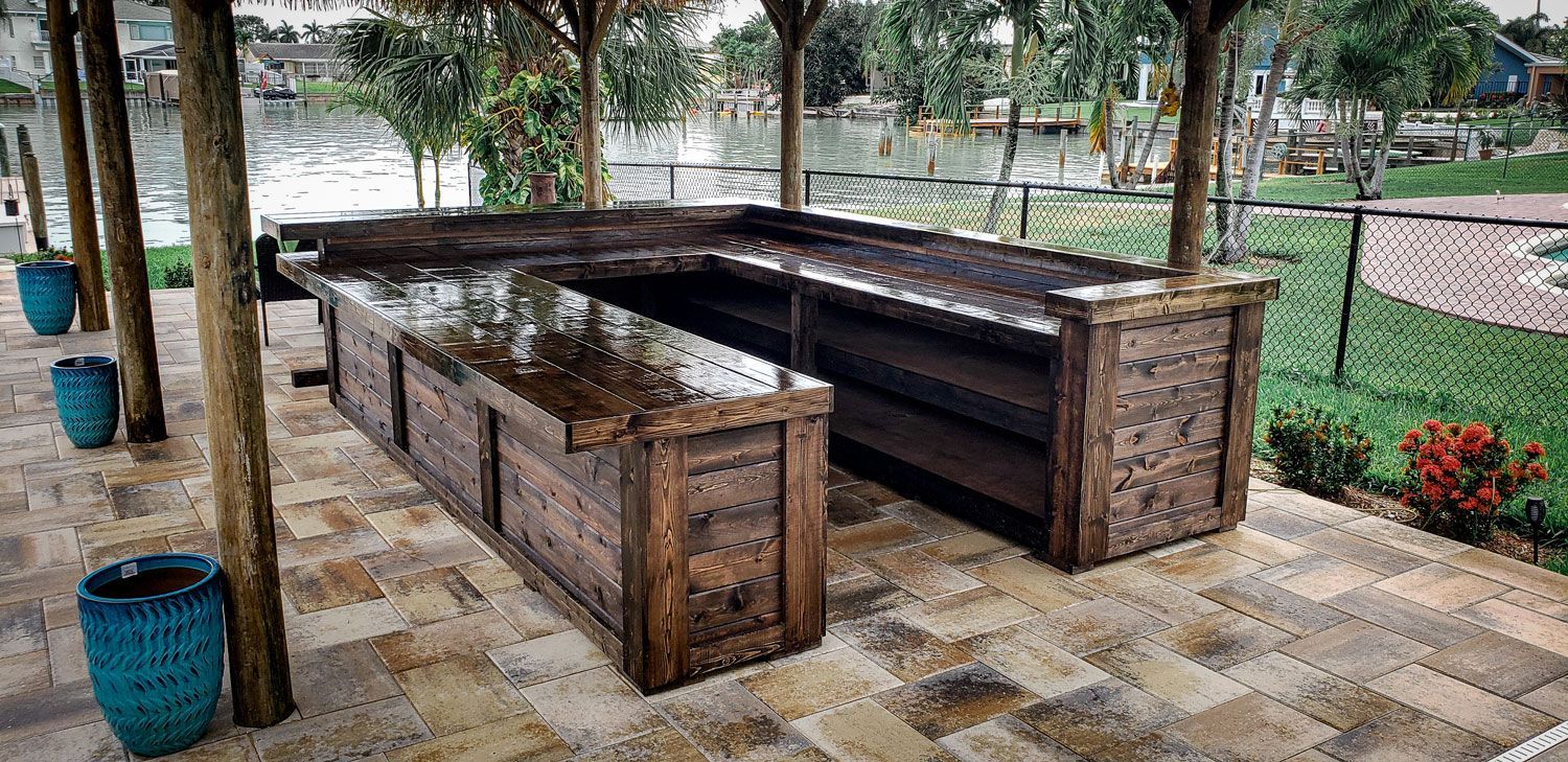 Outdoor wooden U-shaped bar with overhead shelter, near water. Turquoise pots line the left.