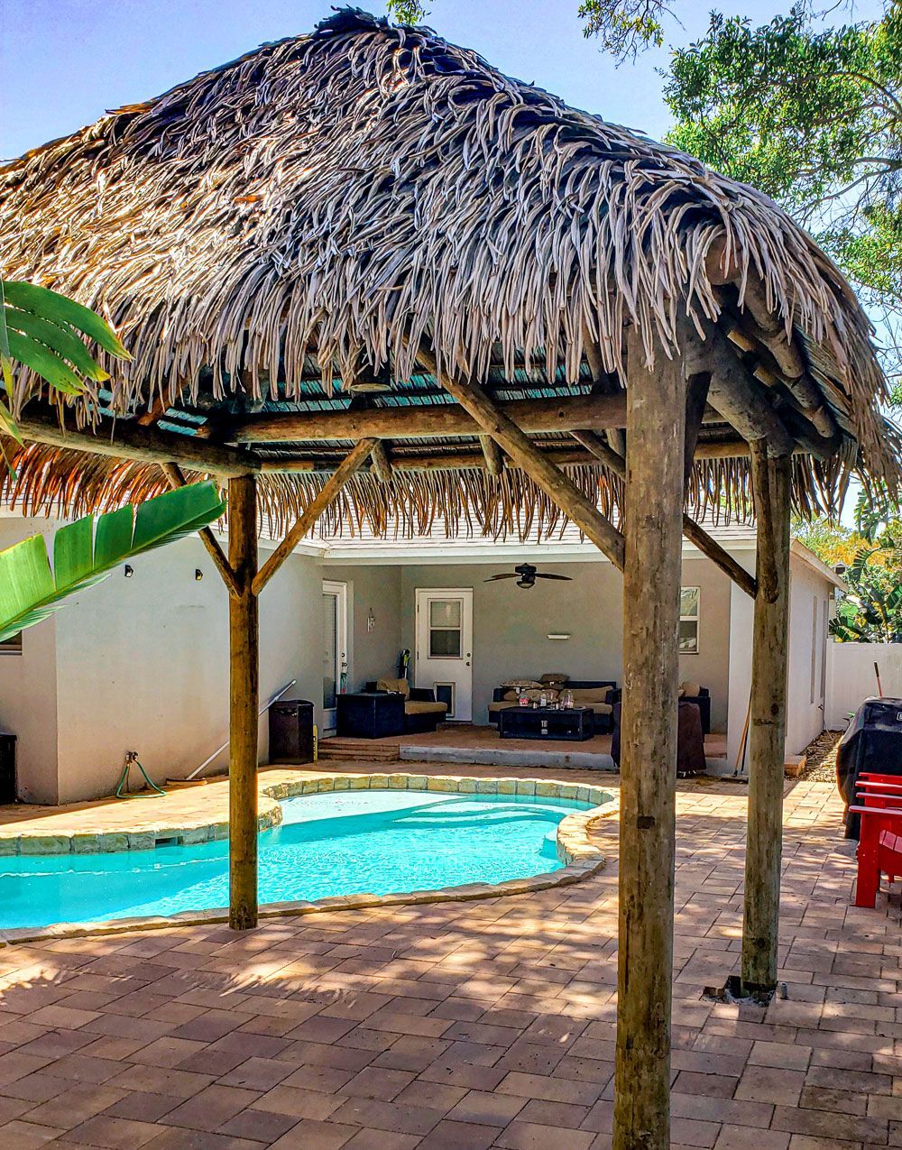 Tiki hut over a pool in a backyard with a house visible in the background.